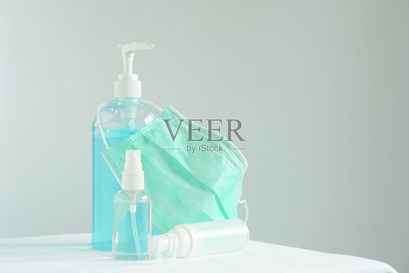 透明塑料瓶内的外科口罩和洗手液凝胶正面,白色桌子上靠墙放置的冠状病毒防护装置。照片摄影图片