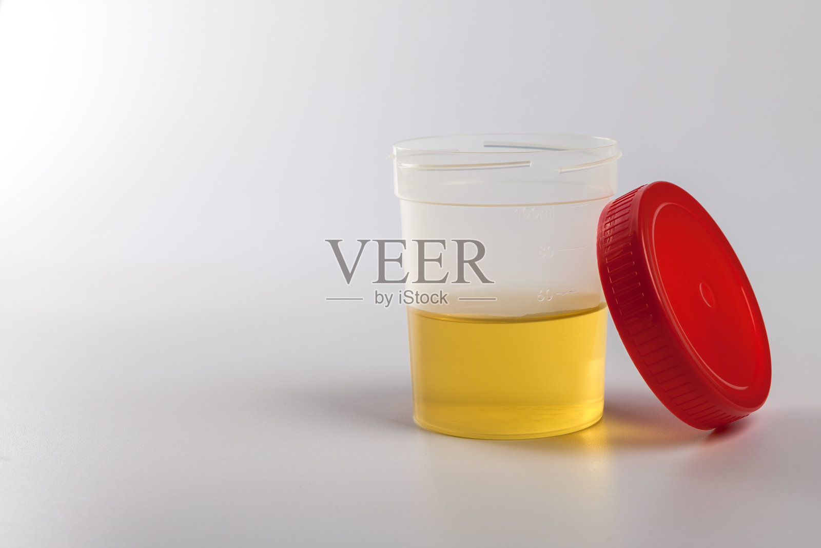 白色背景上的黄色尿检瓶,旁边是红色的开盖照片摄影图片