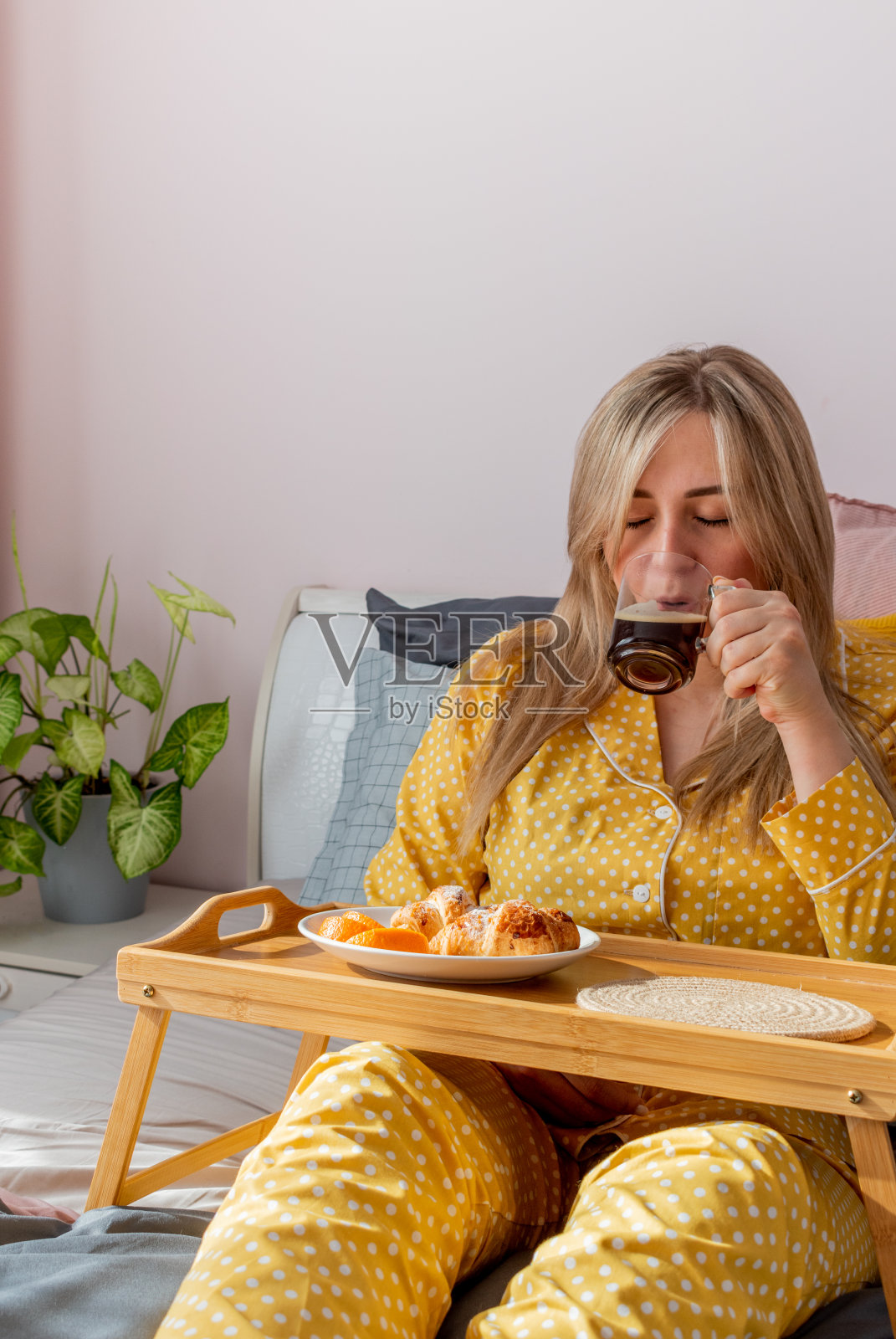 穿着黄色睡衣的年轻女子躺在卧室的床上吃着健康的早餐。照片摄影图片
