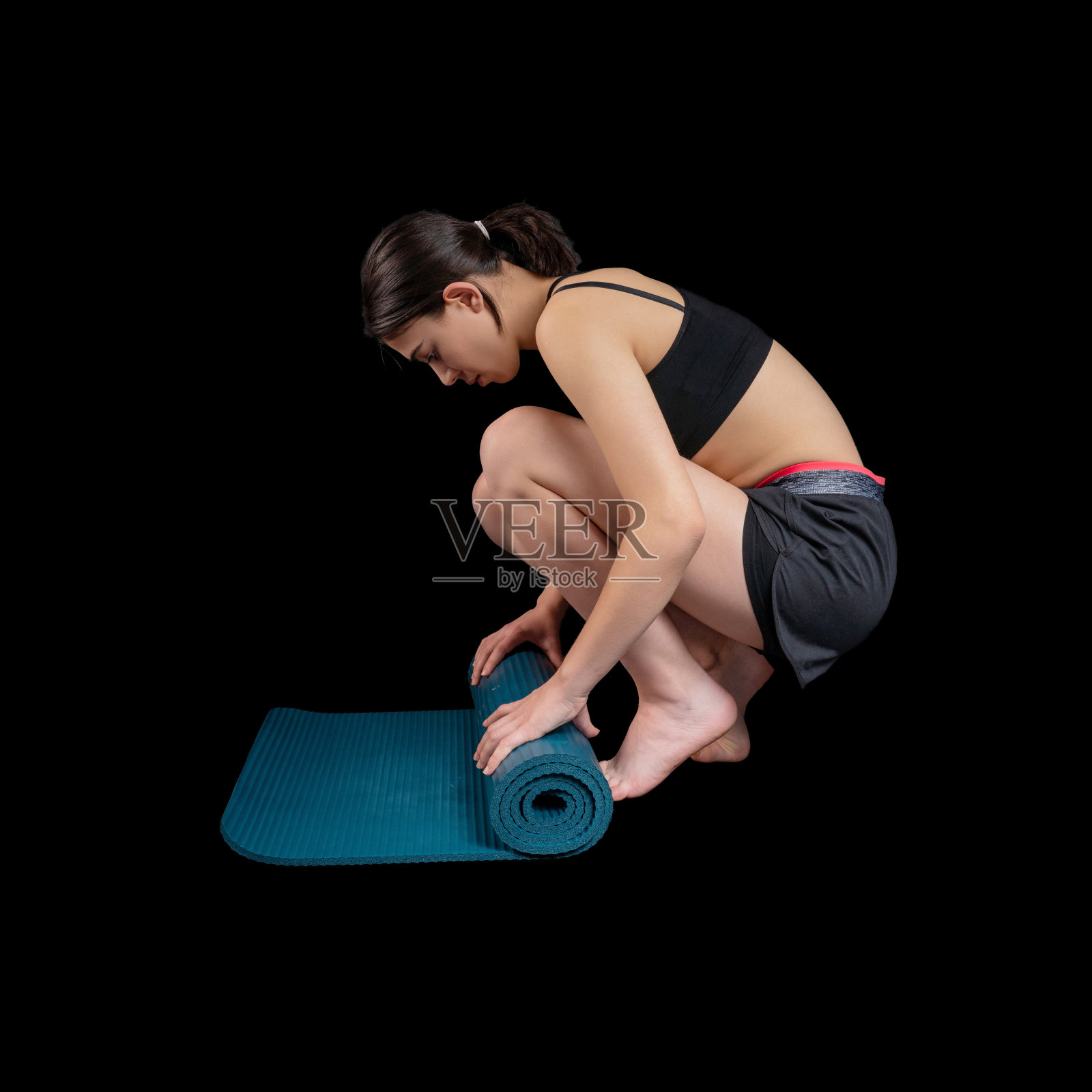 在黑色的背景下,一个年轻女子在做健身训练。照片摄影图片