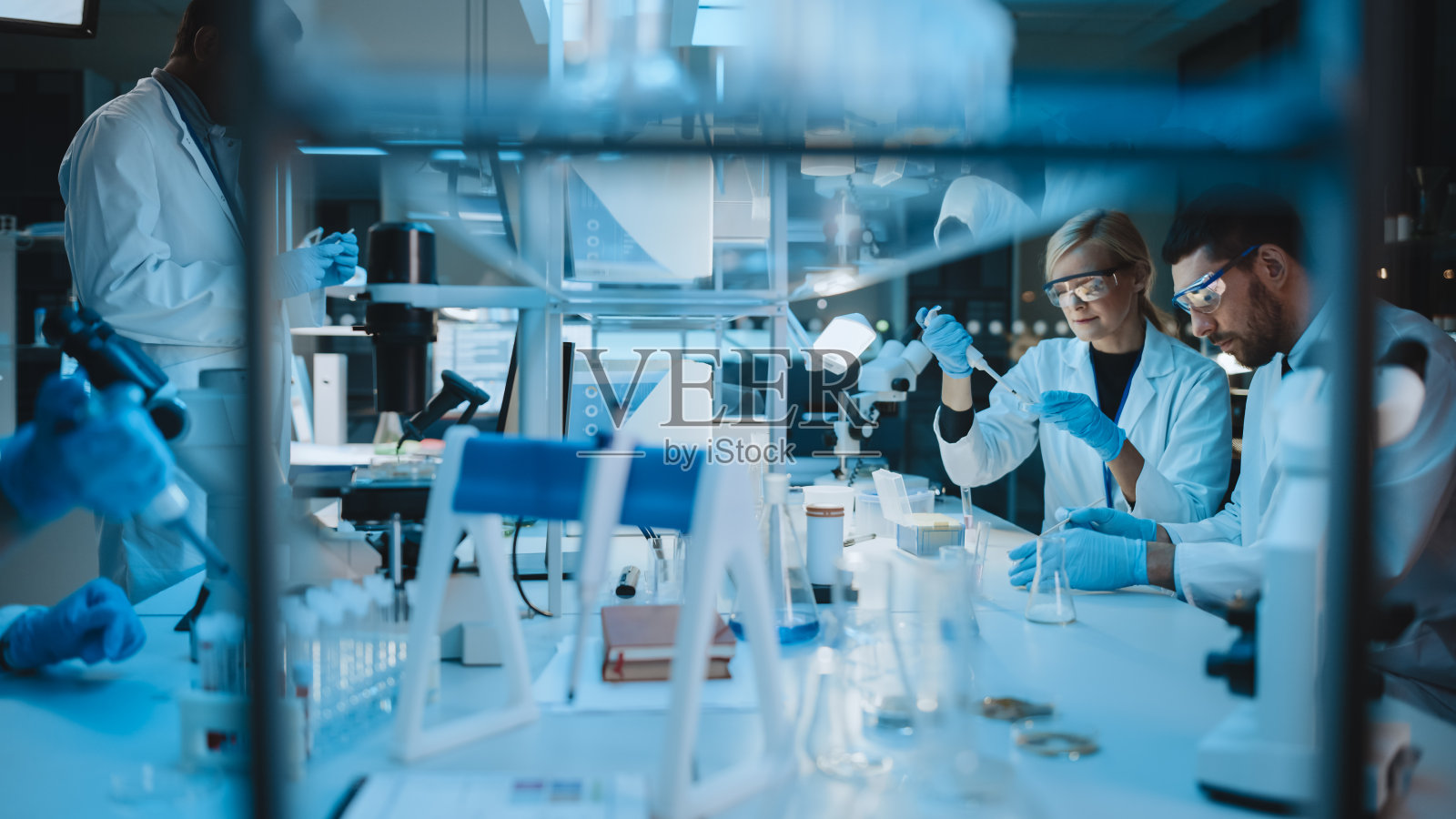 女性和男性医学研究科学家在试管中与液体样品和烧杯中与固体样品进行实验时进行对话。现代科学实验室。照片摄影图片