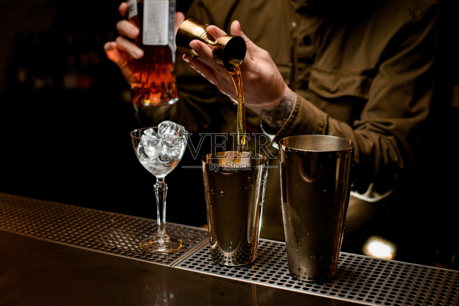 男调酒师将饮料从jigger倒入钢质鸡尾酒调酒器照片摄影图片