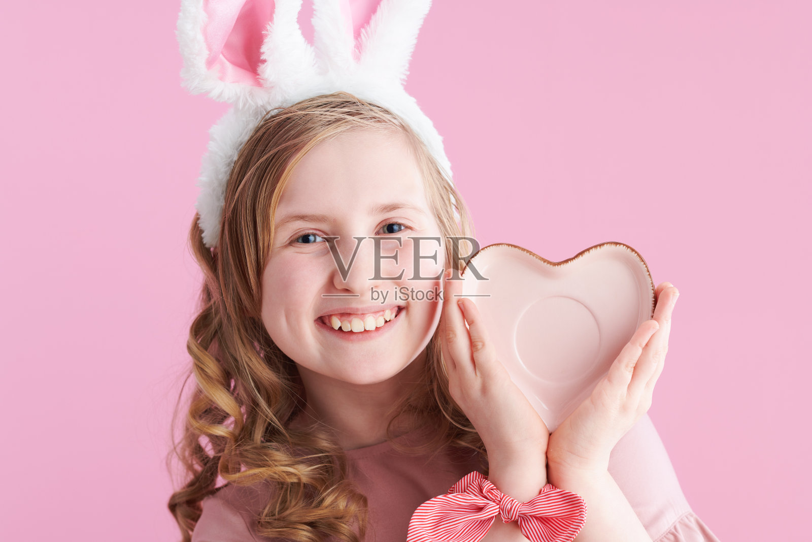 微笑的时尚女孩与长长的卷曲的金色头发在粉红色照片摄影图片