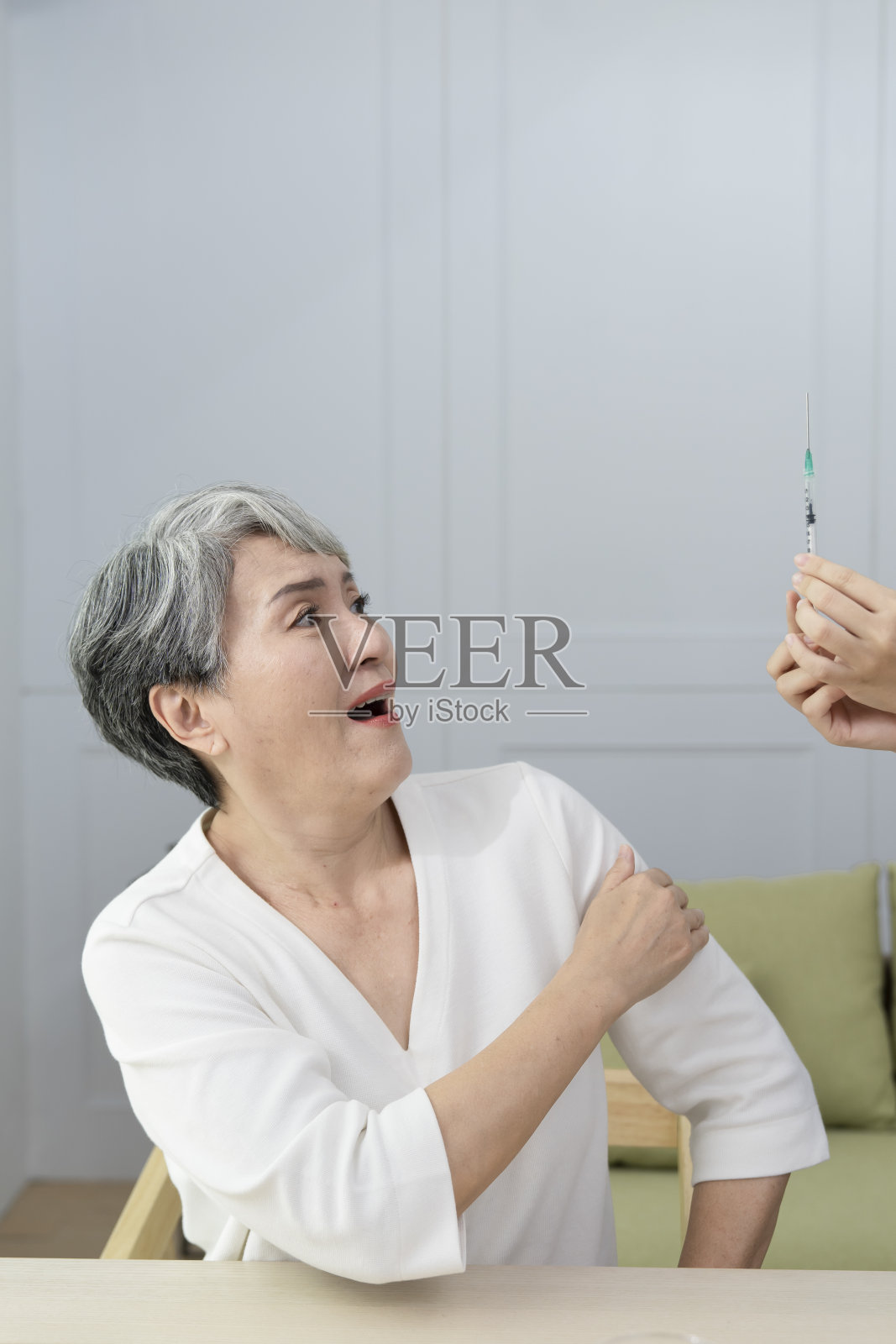 拒绝将疫苗注射到老年妇女的肩膀上,她表现出害怕的表情。照片摄影图片