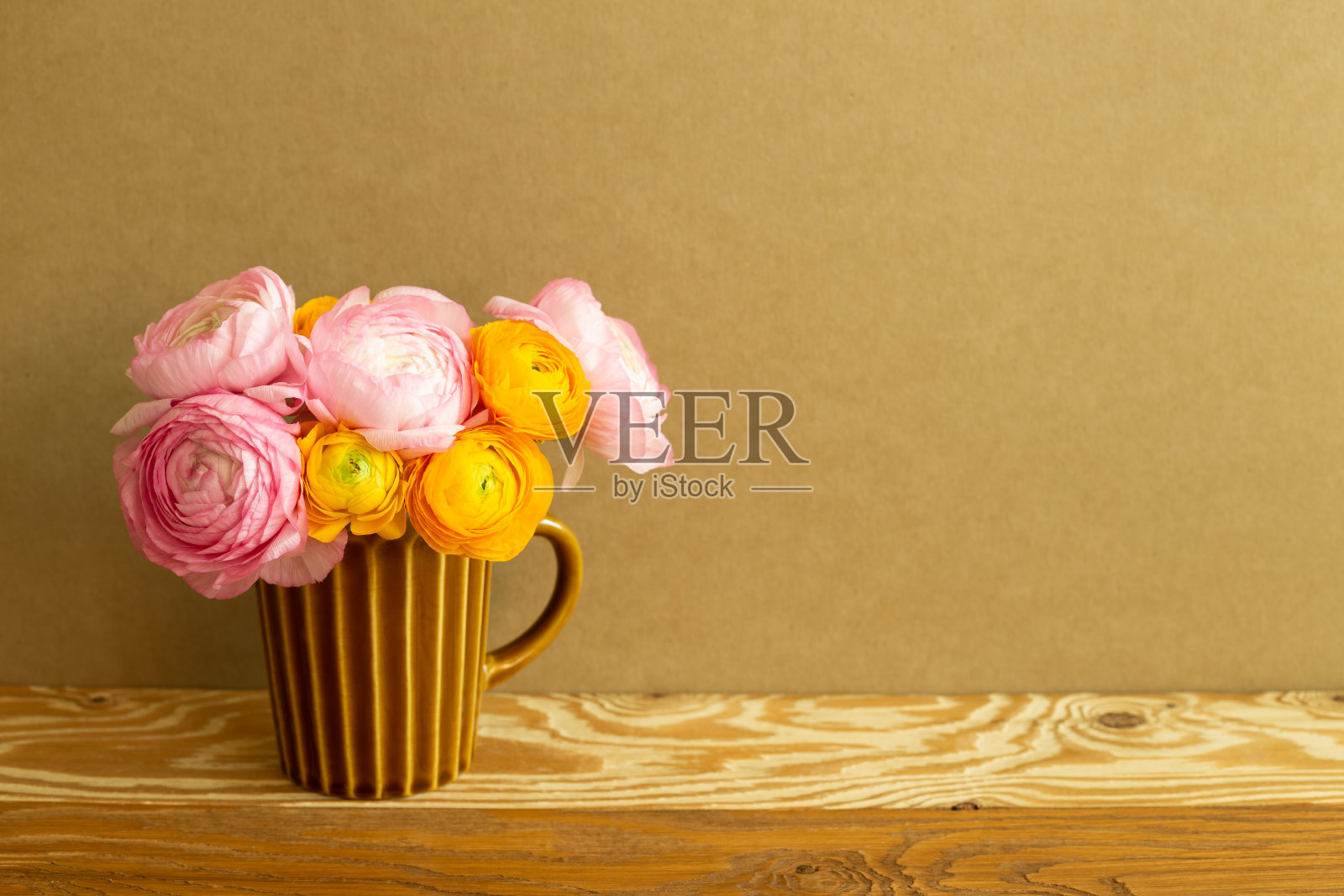 木桌上放着一瓶毛茛花。棕色的背景照片摄影图片