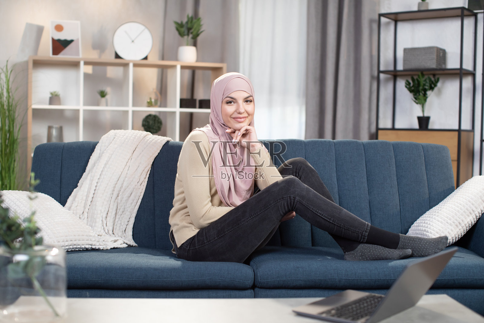 戴着头巾的阿拉伯漂亮女人坐在蓝色沙发上,手托着头,面带微笑地看着镜头照片摄影图片