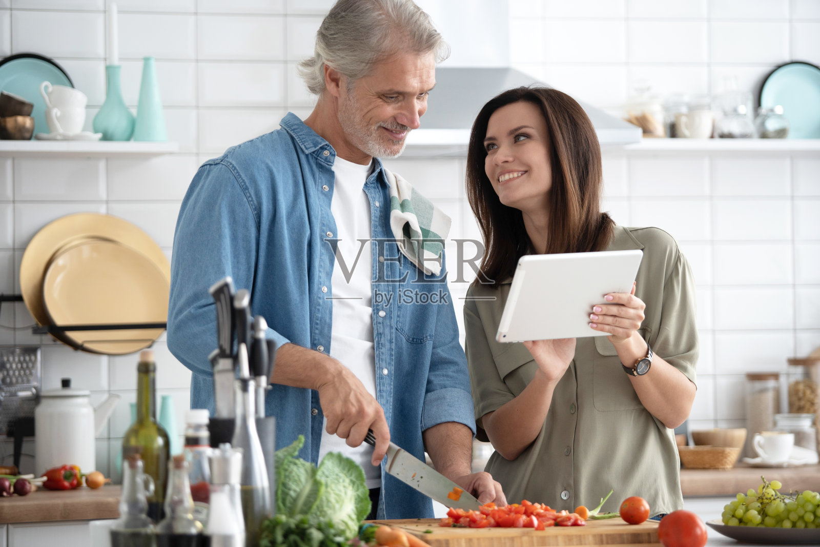 一对美丽的夫妇在厨房里微笑着用数码平板电脑做饭。照片摄影图片