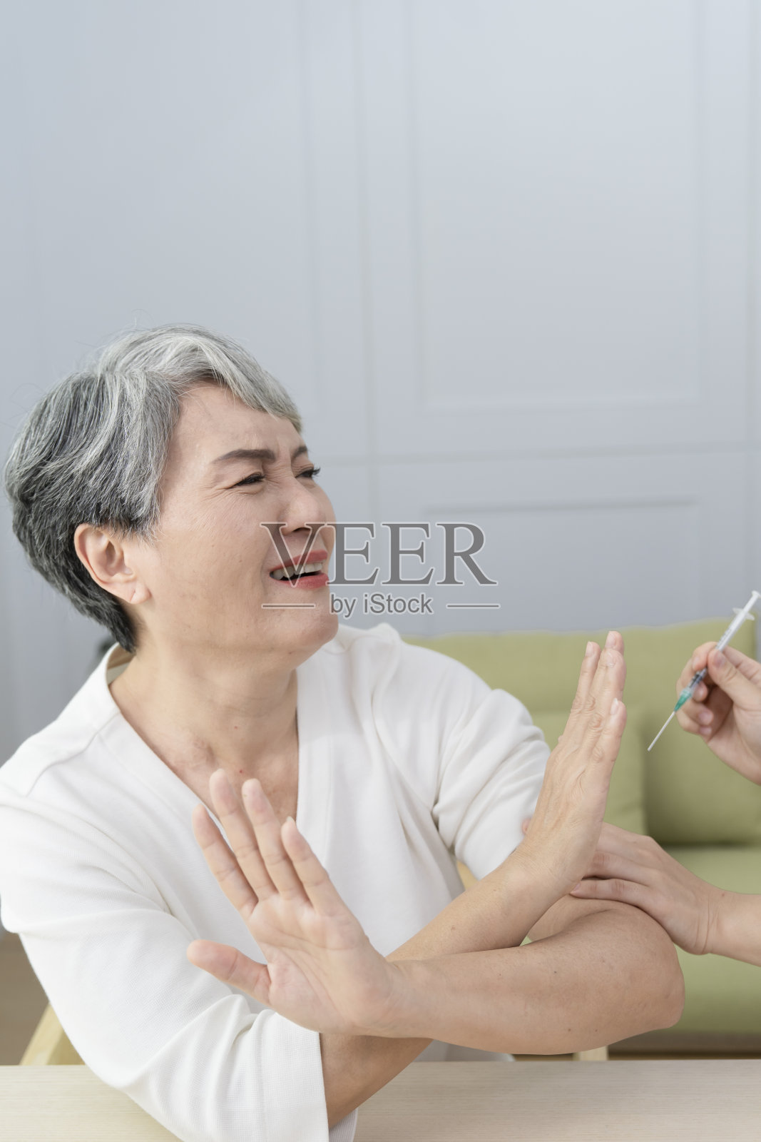 拒绝将疫苗注射到老年妇女的肩膀上,她表现出害怕的表情。照片摄影图片