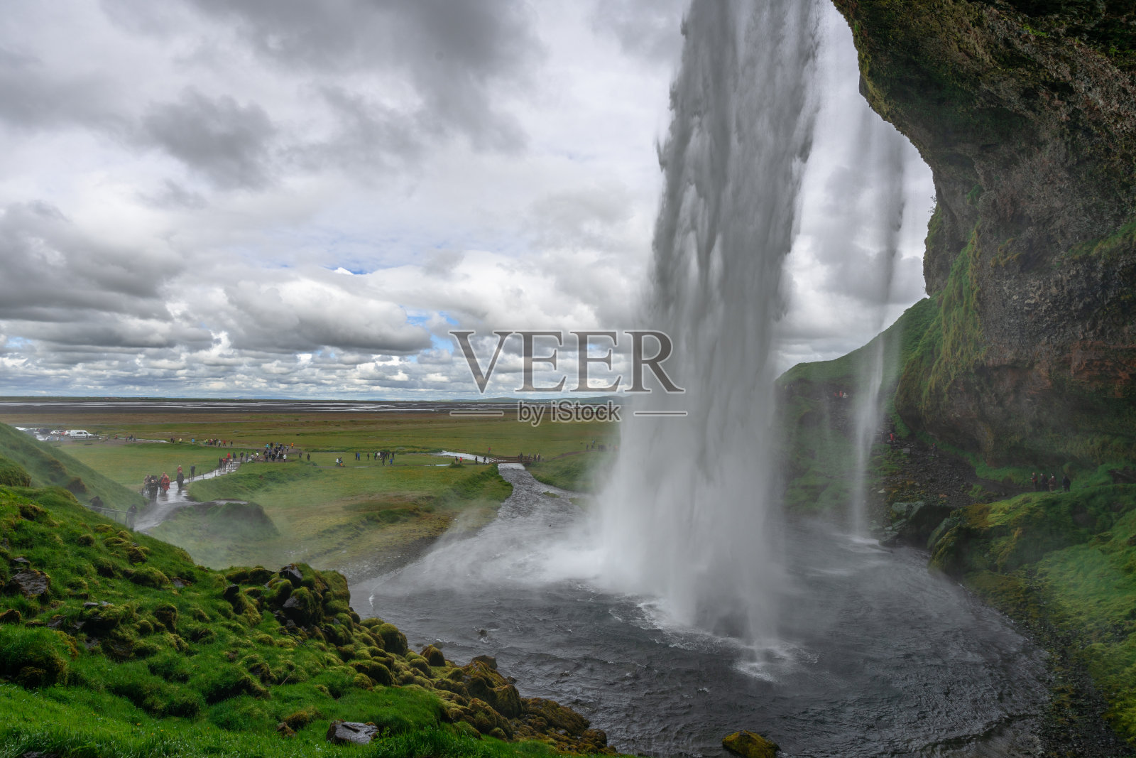 在阴天从冰岛的Seljalandsfoss瀑布后面观看。照片摄影图片