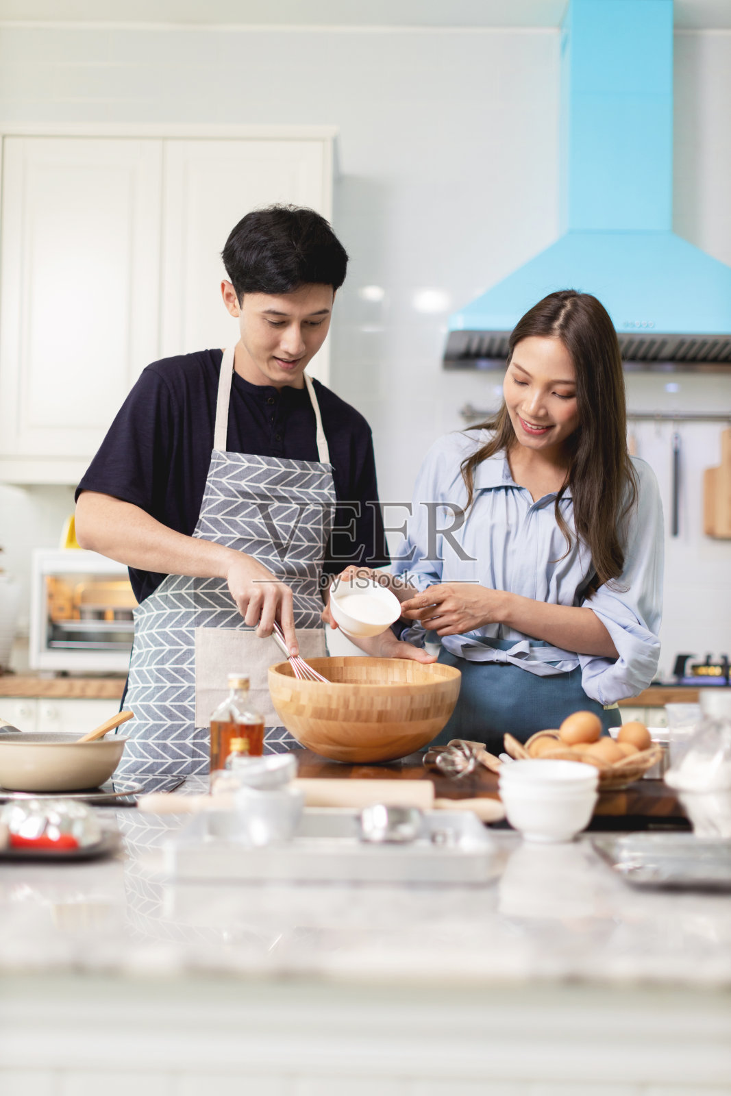 在家里的厨房里营造浪漫的气氛。年轻人一起在木碗里搅拌各种材料,然后再一起搅拌。照片摄影图片