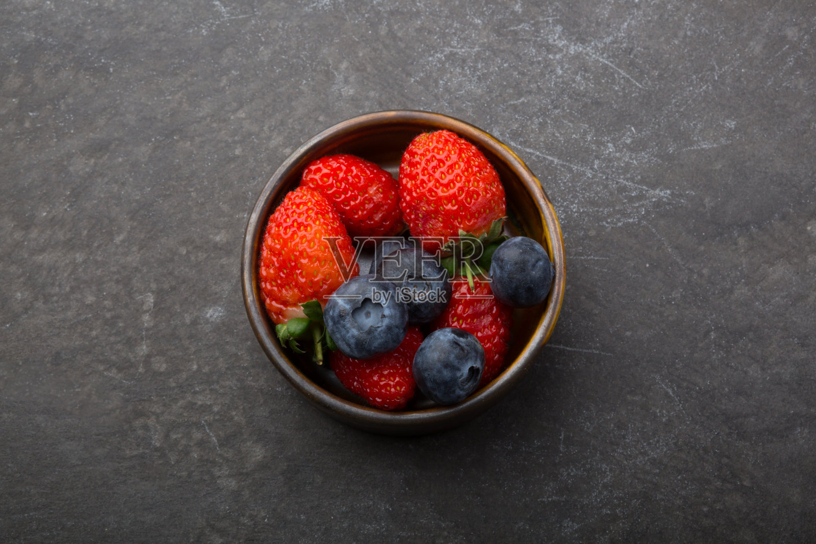 黑桌子上有一个小杯子,里面装着草莓和蓝莓照片摄影图片