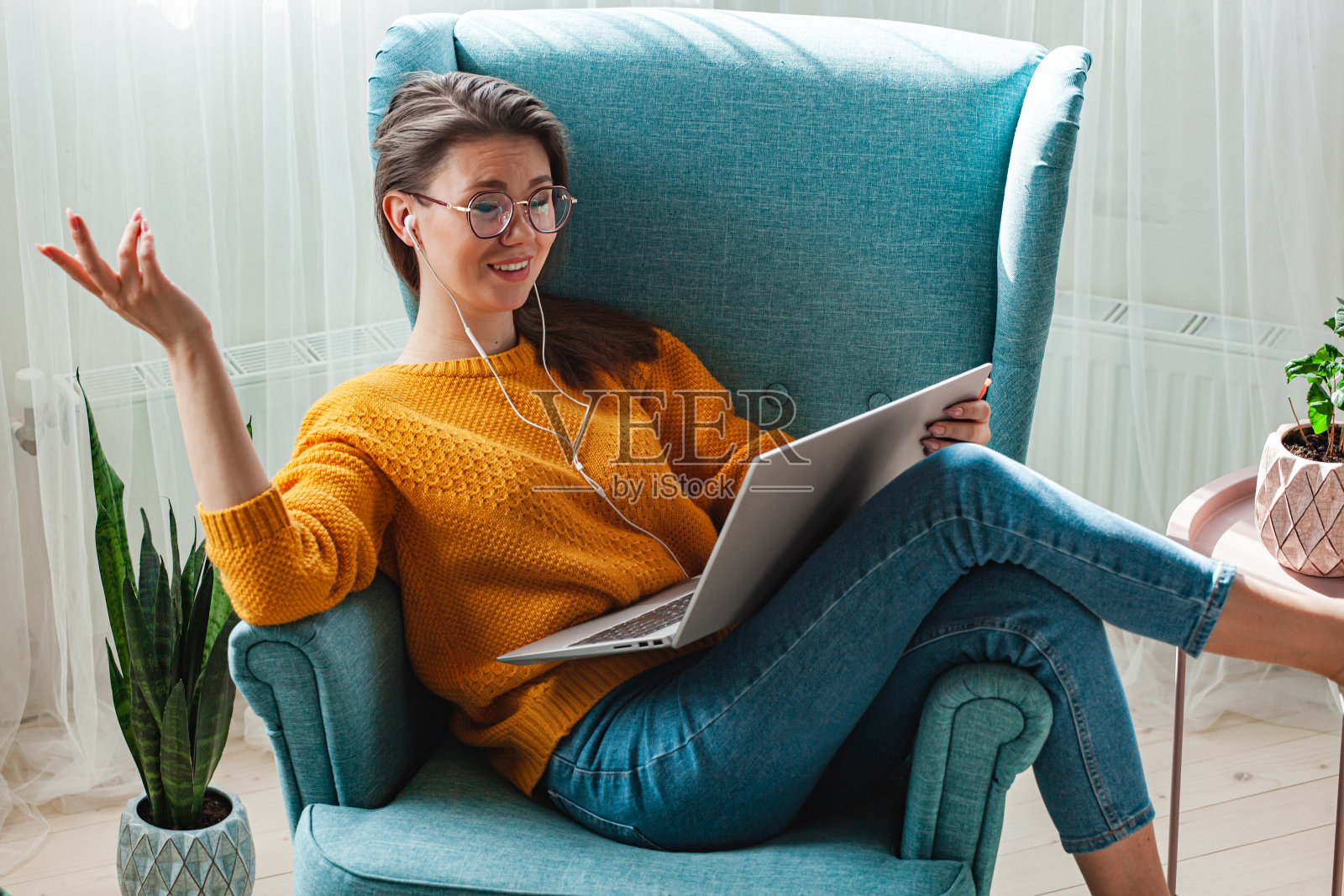 年轻女子躺在家里的扶手椅上使用笔记本电脑和耳机照片摄影图片