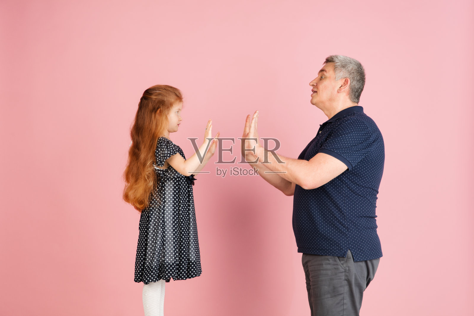 两个人,男人和小女孩,爸爸和女儿孤立在粉红色的背景下。照片摄影图片