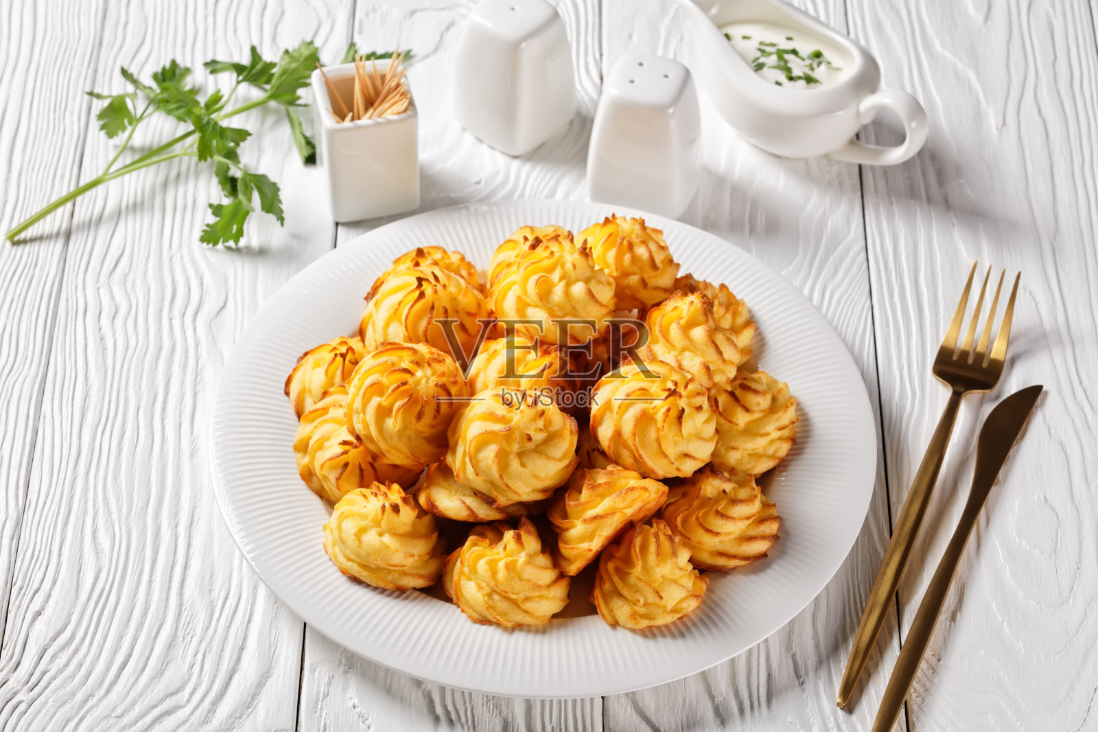 公爵夫人土豆,土豆泥呈装饰性的漩涡状,在烤箱中呈棕色,配以白色酱汁,放在木桌上的白色盘子里,配有金色的餐具照片摄影图片