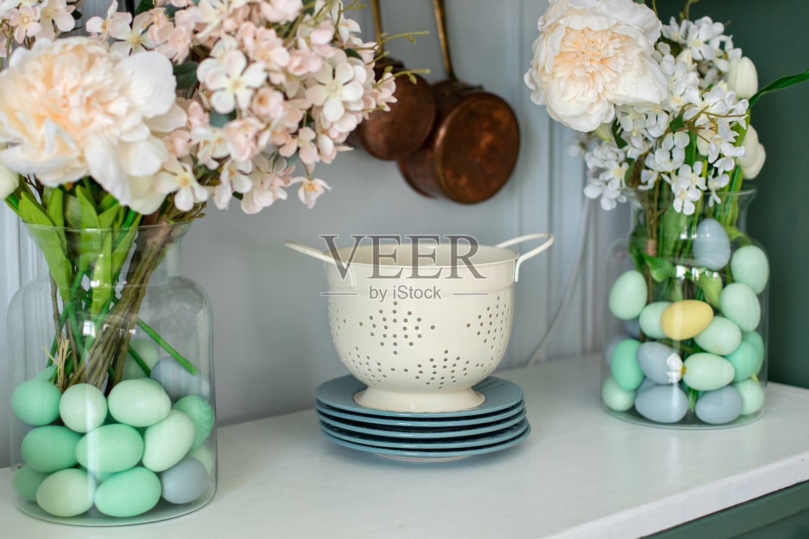 台面的正面视图与厨房工具,用具。春季厨房室内装饰。搪瓷的白色滤锅,盘子,花瓶里的鲜花和餐桌上的复活节彩蛋。厨房的组织照片摄影图片