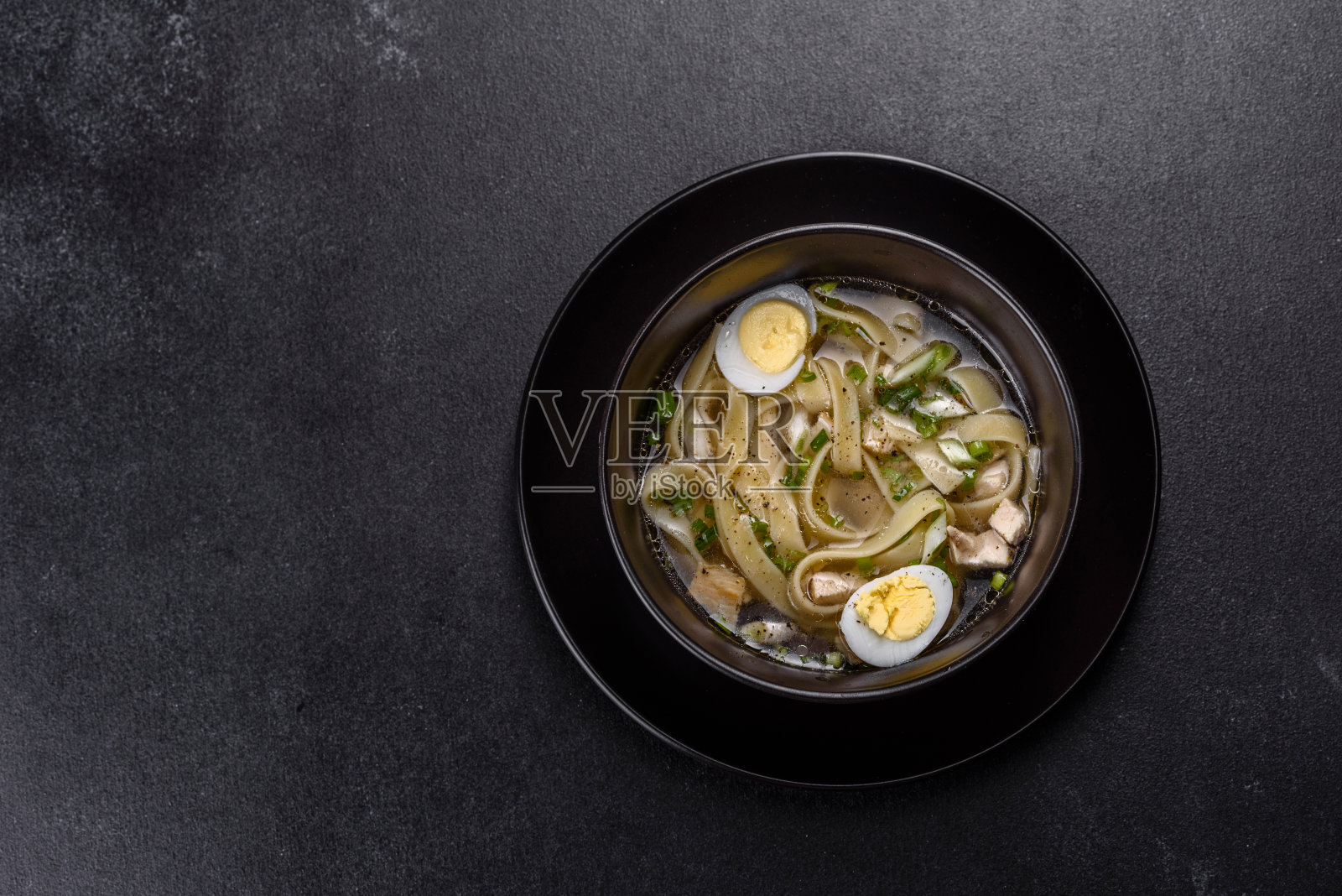 新鲜美味的热汤,面条和鹌鹑蛋在一个黑色的盘子照片摄影图片