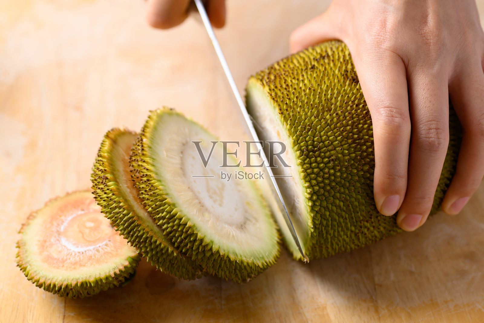 手拿小菠萝蜜,用菜刀在木板上切照片摄影图片