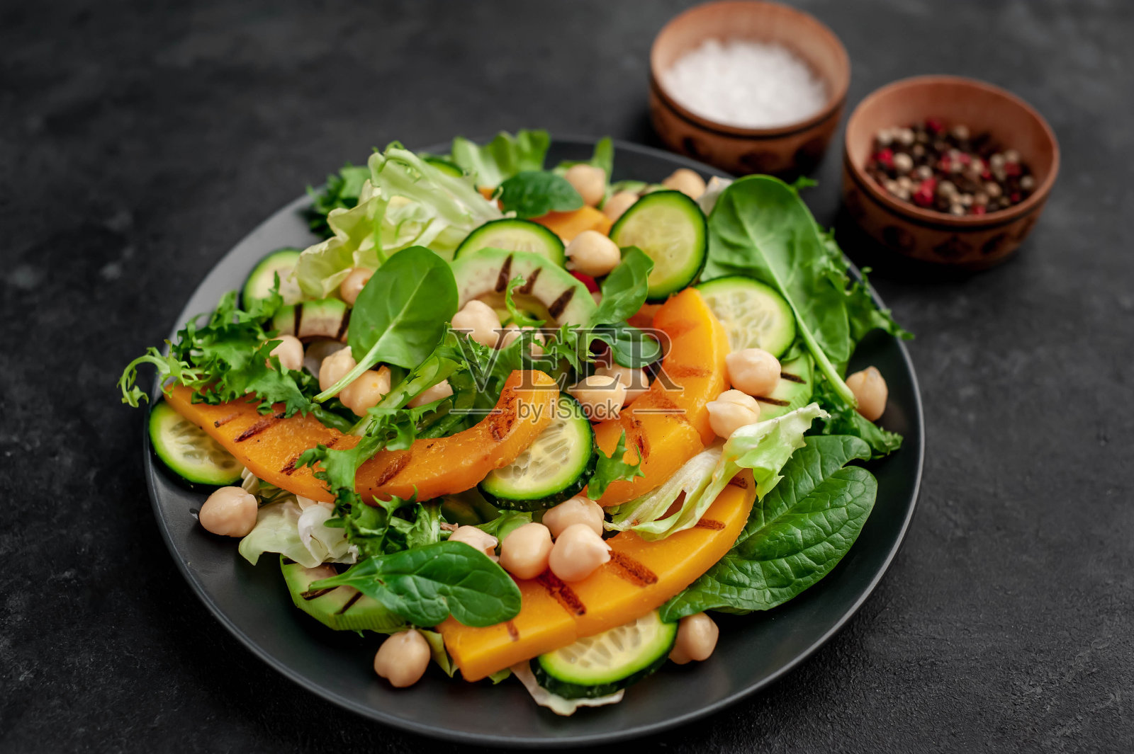 石头背景上放着一盘南瓜沙拉、鳄梨、黄瓜、鹰嘴豆和莴苣。照片摄影图片