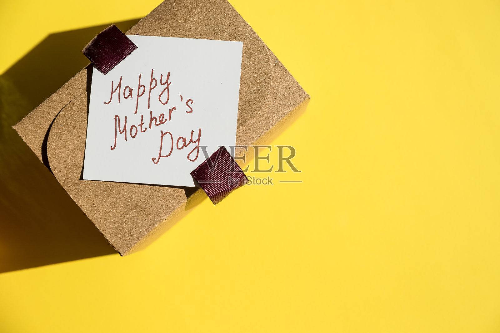 一个牛皮纸盒子里的礼物,在明亮的背景上有蝴蝶结。给你的爱人一个惊喜。母亲节的概念。时尚的礼物盒子。副本的空间。母亲节的信息照片摄影图片