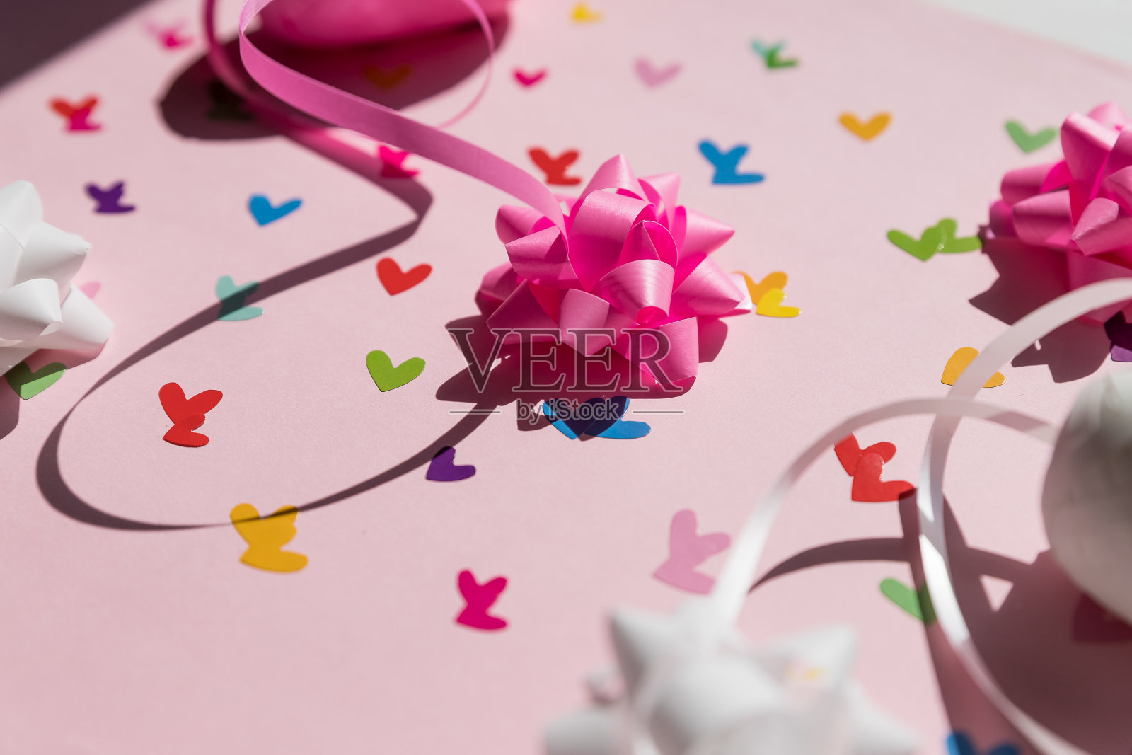 美丽多彩的心,白色和粉红色的节日蝴蝶结在粉红色的背景。庆祝的概念。节日背景为情人节,婚礼。绸缎蝴蝶结和缎带照片摄影图片