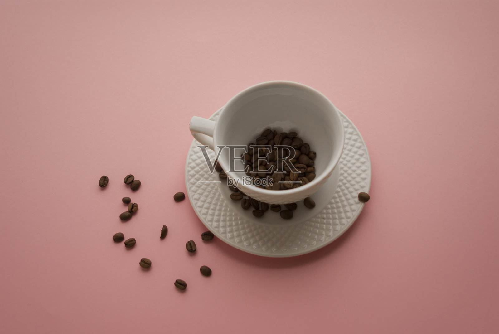 白色的杯碟和黑色的咖啡豆在明亮的粉红色背景上照片摄影图片