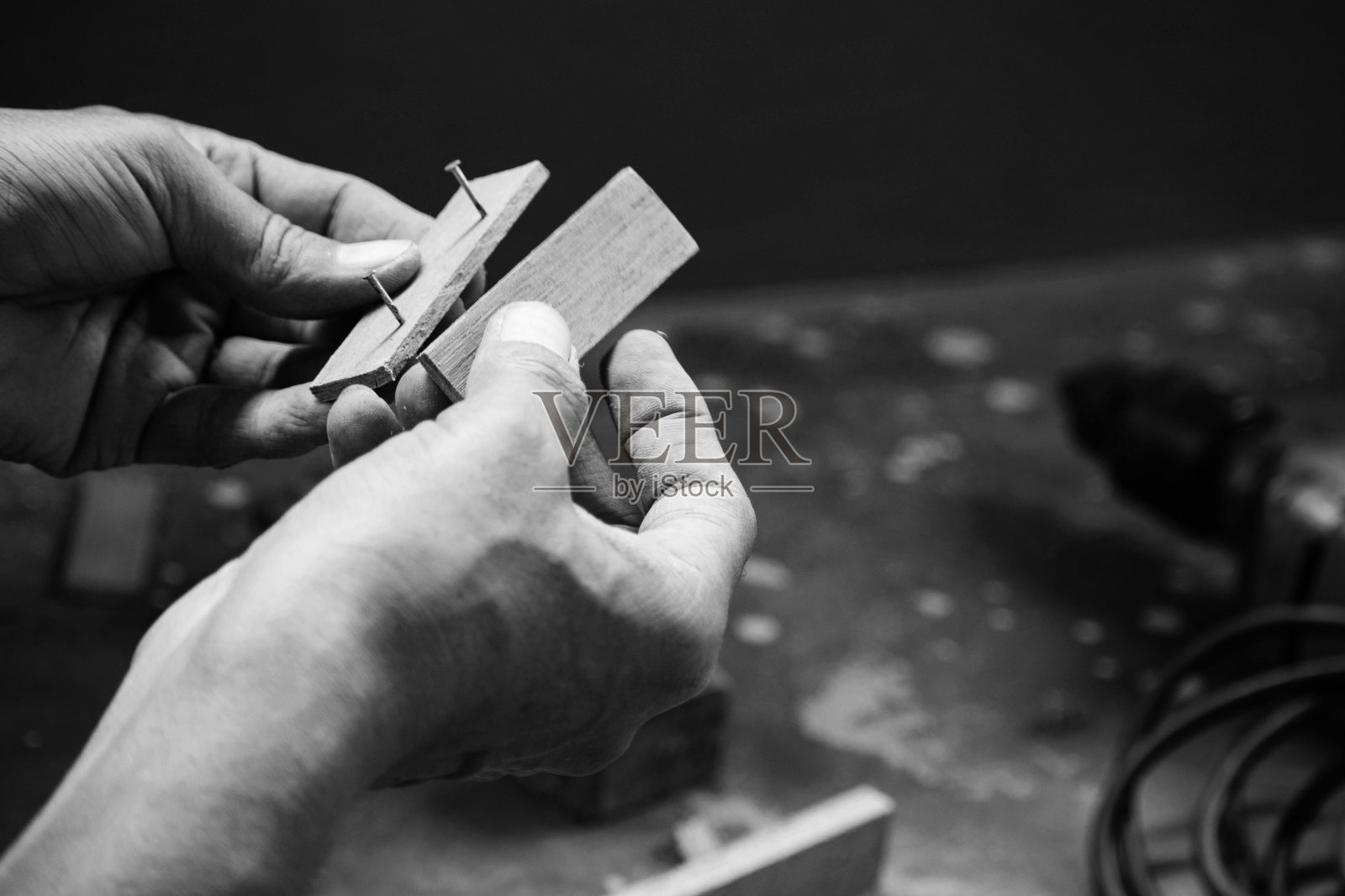 机修工用木头和其他工具做木工活。他正在用锤子把钉子的头敲成木片,用锯子锯木棒。他旁边的地板上放着一台钻床。照片摄影图片