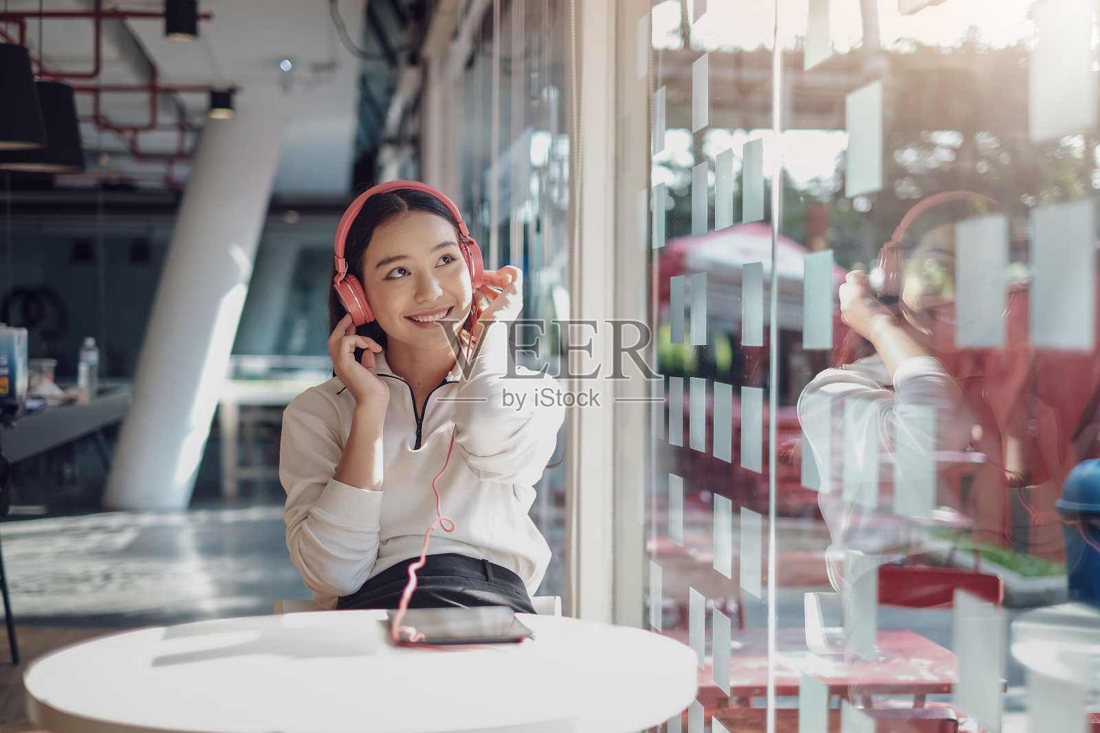 漂亮的亚洲女人戴着耳机,坐在大窗户边欣赏音乐。照片摄影图片