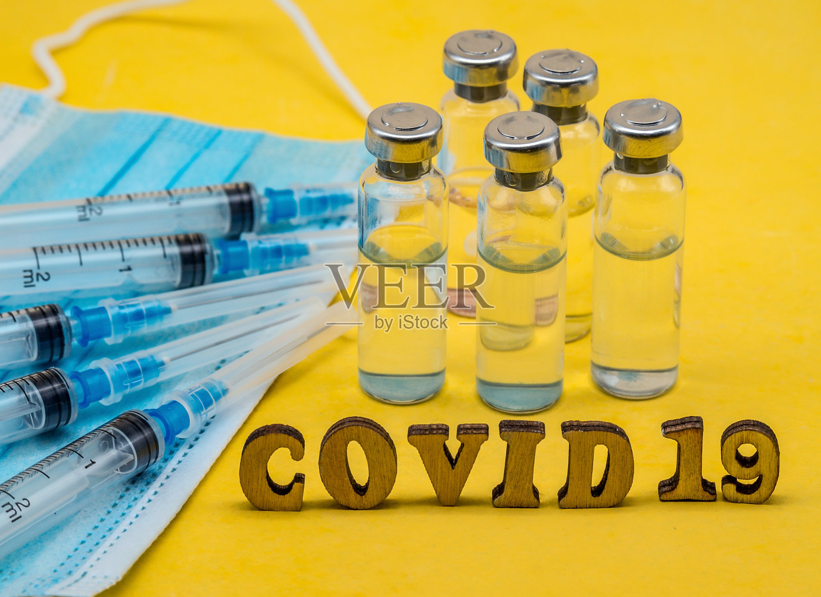 黄色背景上有医用安瓿、注射器和口罩。疫苗接种covid-19。照片摄影图片