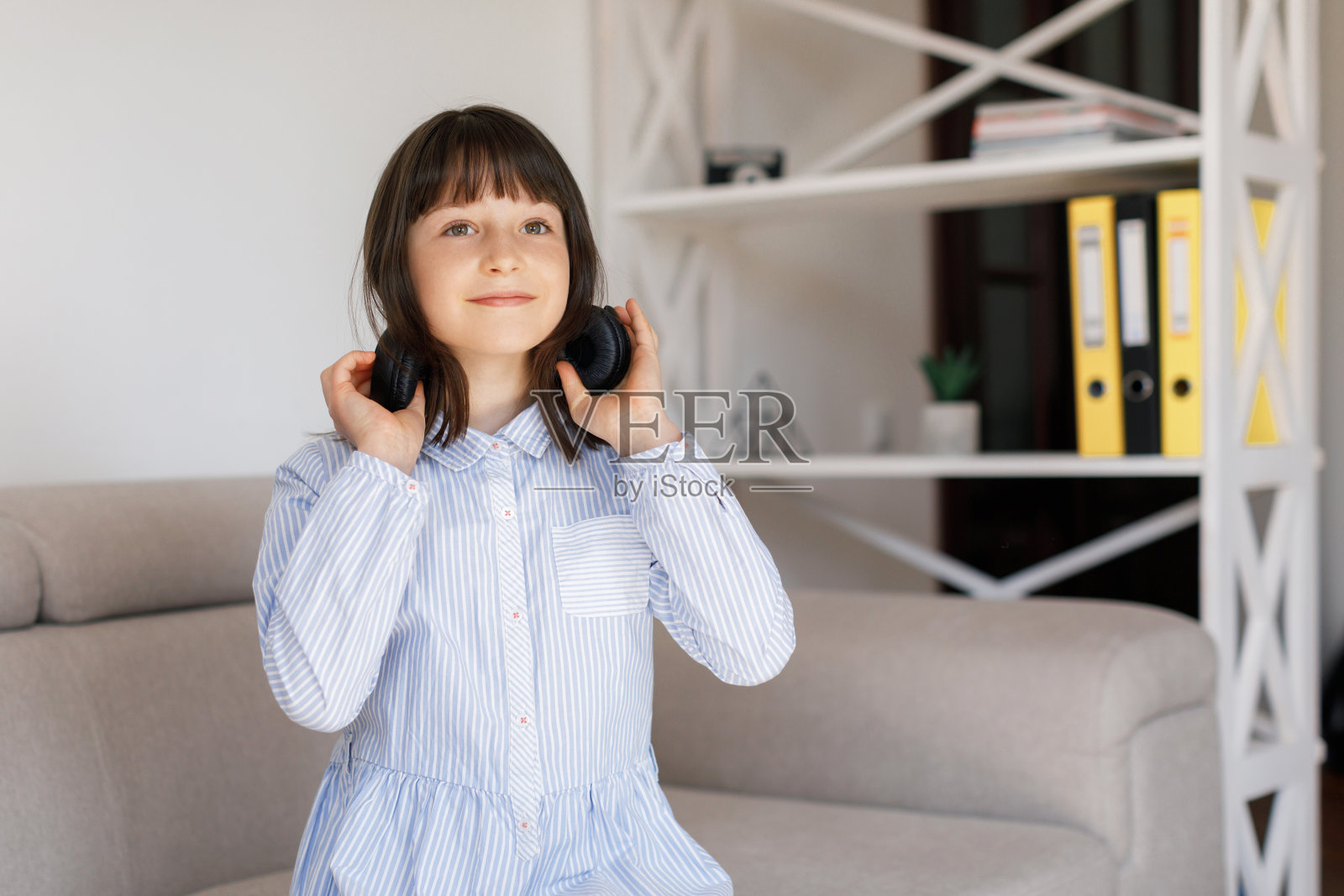 快乐有趣的少女带着黑色头发戴耳机站在房间里听新的流行音乐,享受,唱歌,放松在舒适的客厅在家里。照片摄影图片