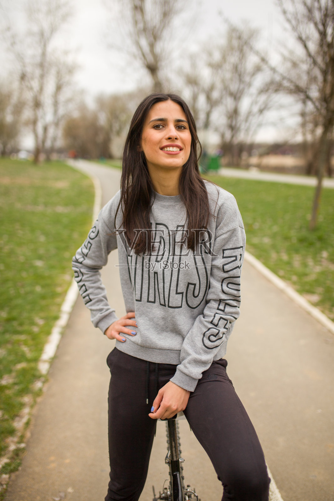 一个年轻女子,摆姿势,看着相机坐在自行车上。照片摄影图片