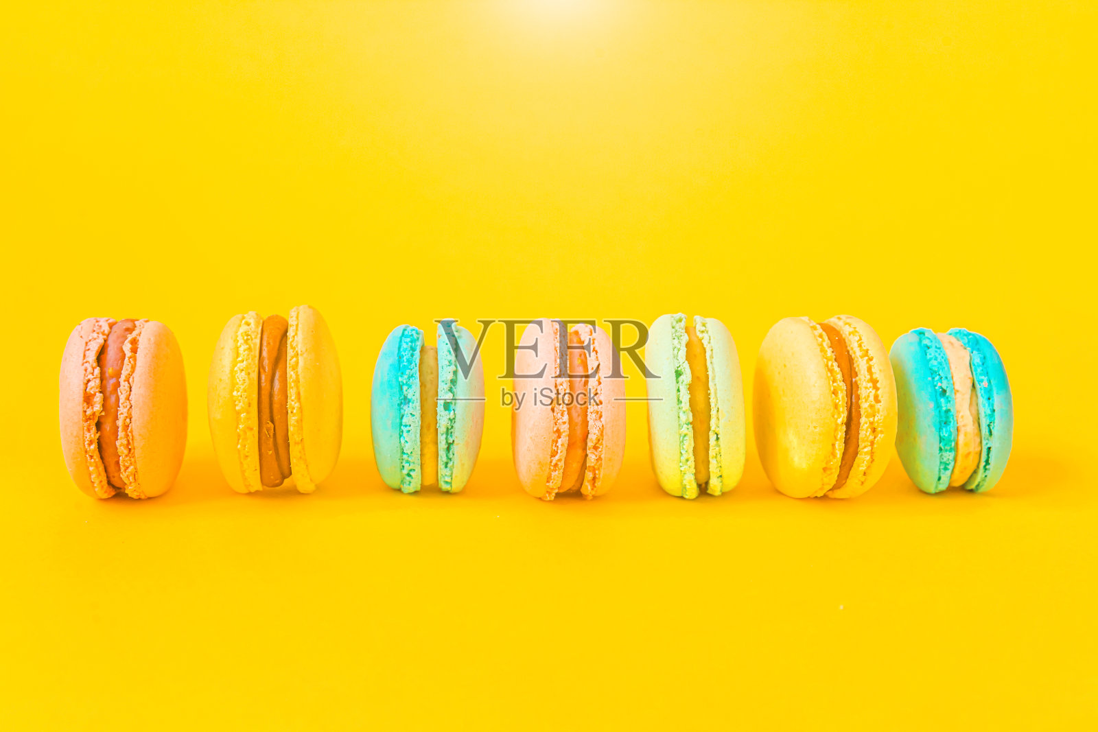 甜杏仁七彩独角兽粉蓝黄绿马卡龙或马卡龙甜品蛋糕孤立在时髦的黄色现代时尚背景下。法国甜的饼干。最小的食品烘焙概念复制空间照片摄影图片