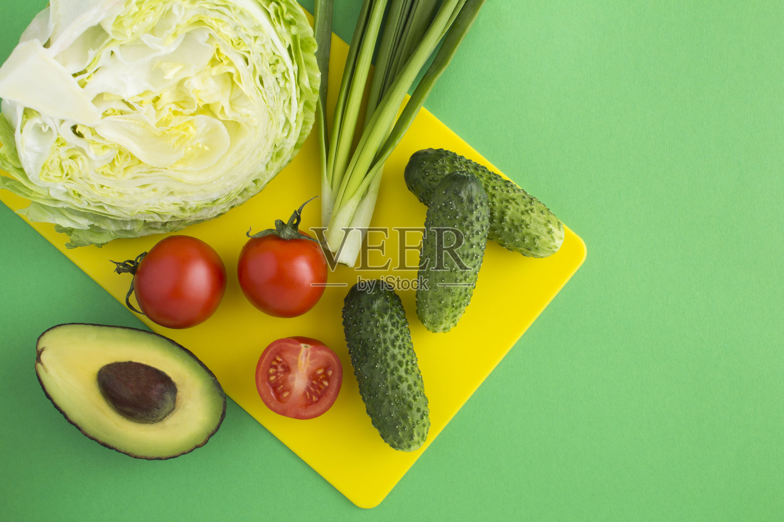 绿色背景的黄色砧板上放着沙拉的配料。健康食品。前视图。副本的空间。照片摄影图片