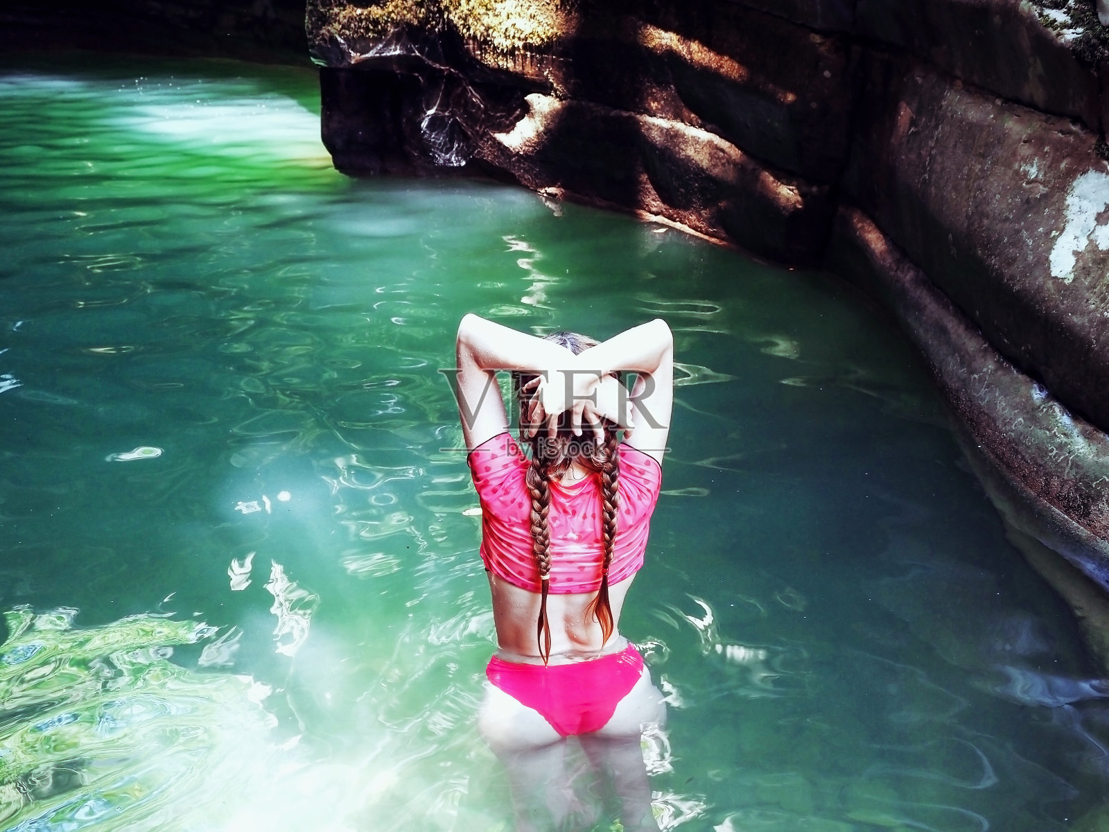 一个扎着辫子的女孩站在耀眼的阳光下,在岩石峡谷中流淌的碧绿的河水中照片摄影图片
