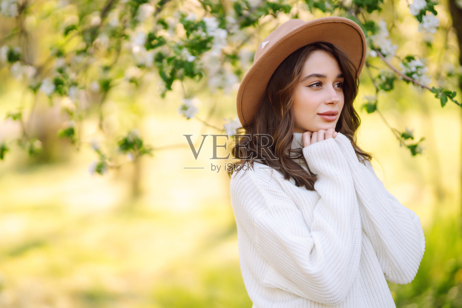 微笑的女人与帽子摆姿势在盛开的春天公园。放松、旅游、自由、春假的概念。时尚风格。照片摄影图片