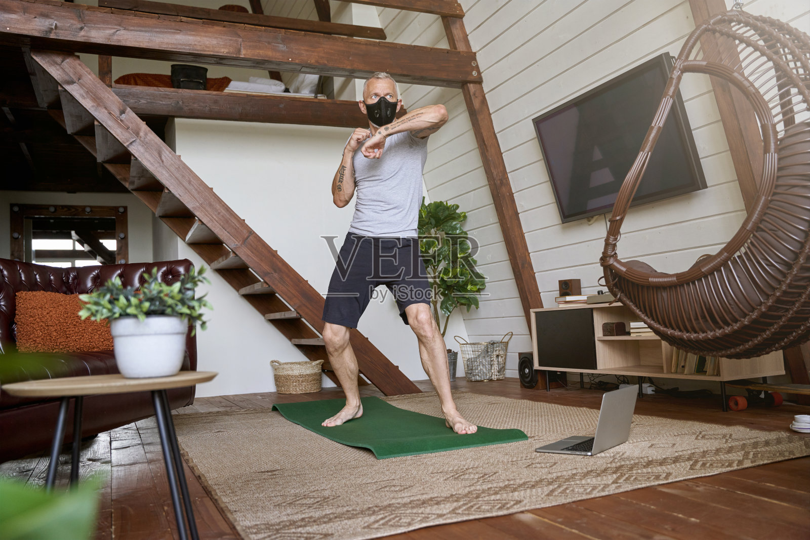 活跃的中年男子戴着面罩站在拳击姿势,在家锻炼,在笔记本电脑上看在线锻炼。新冠肺炎期间的体育运动照片摄影图片