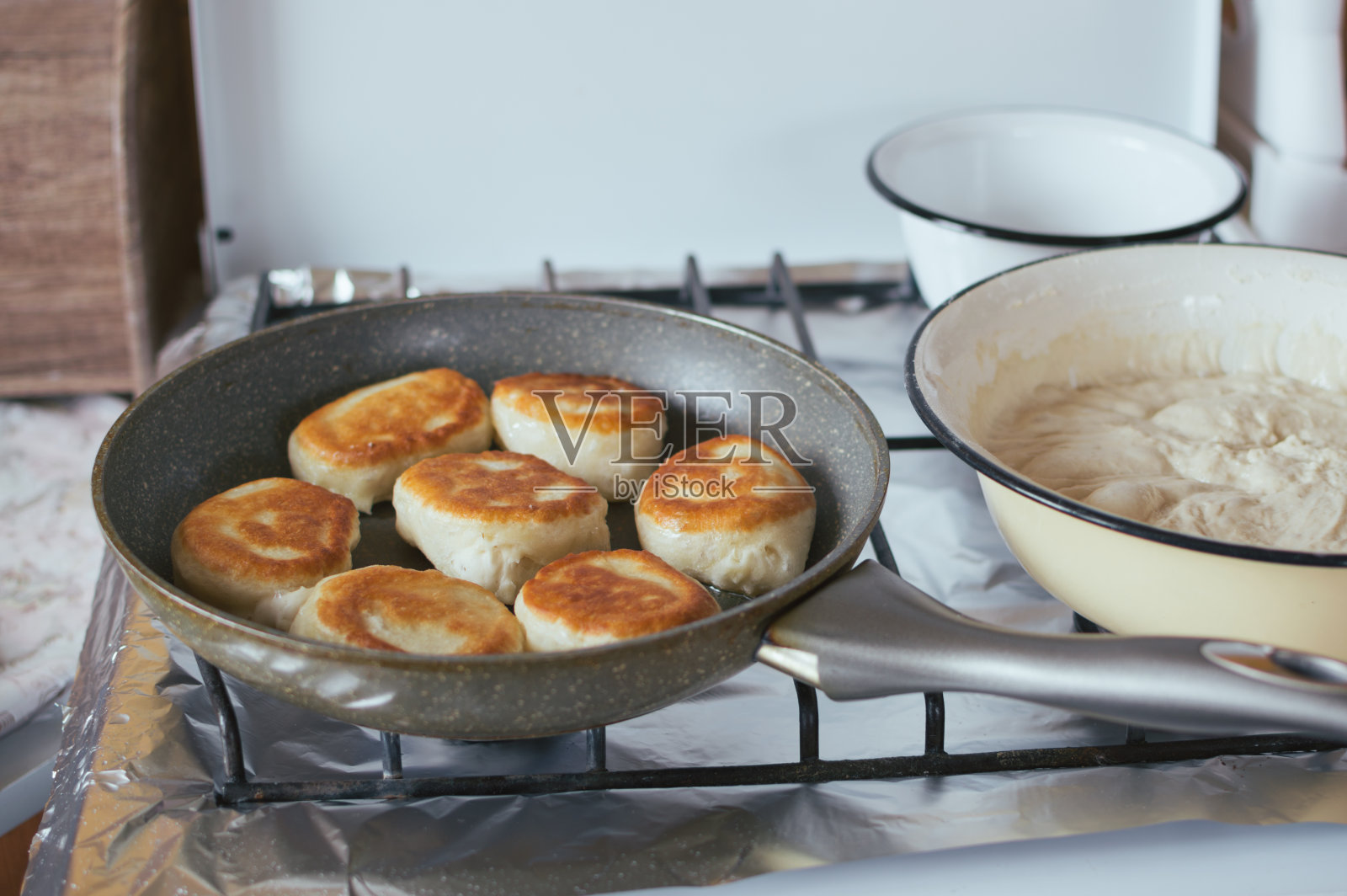发酵薄煎饼是在炉子上的煎锅里煎的。面团在碗里照片摄影图片