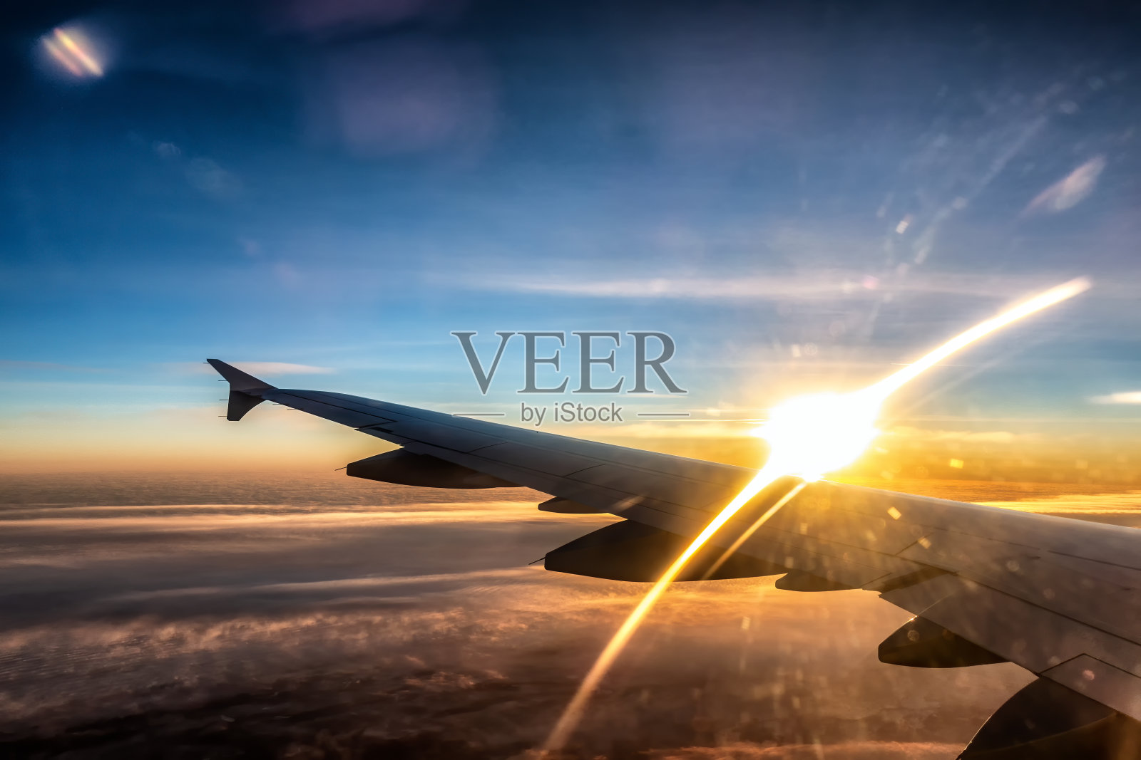 客机左翼视图。夕阳在机翼上闪耀着金色的光芒。金色的阳光照亮了飞机下面的厚厚的云层。乘客窗口的水平视图照片摄影图片