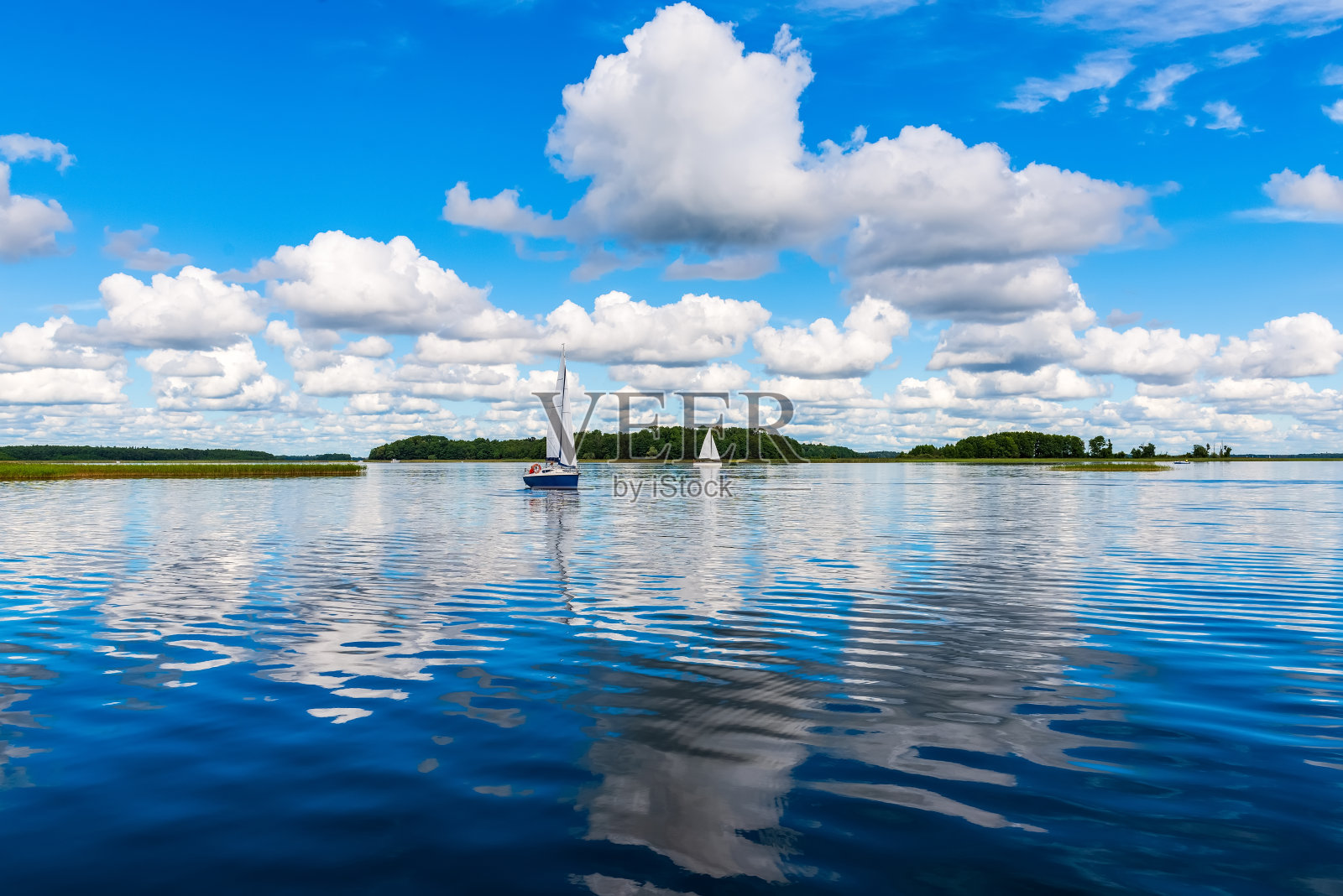 在蓝天白云的映衬下,游艇在湖面上航行。乘帆船在湖上度假。照片摄影图片