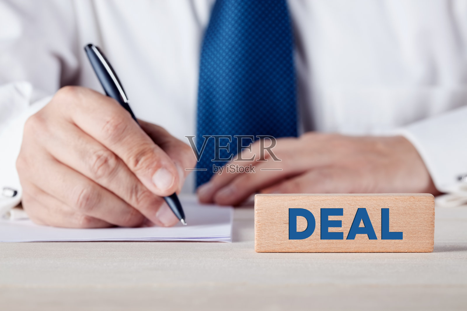 “交易”这个词写在一块木块上,背景是一个商人在签署一份文件。照片摄影图片