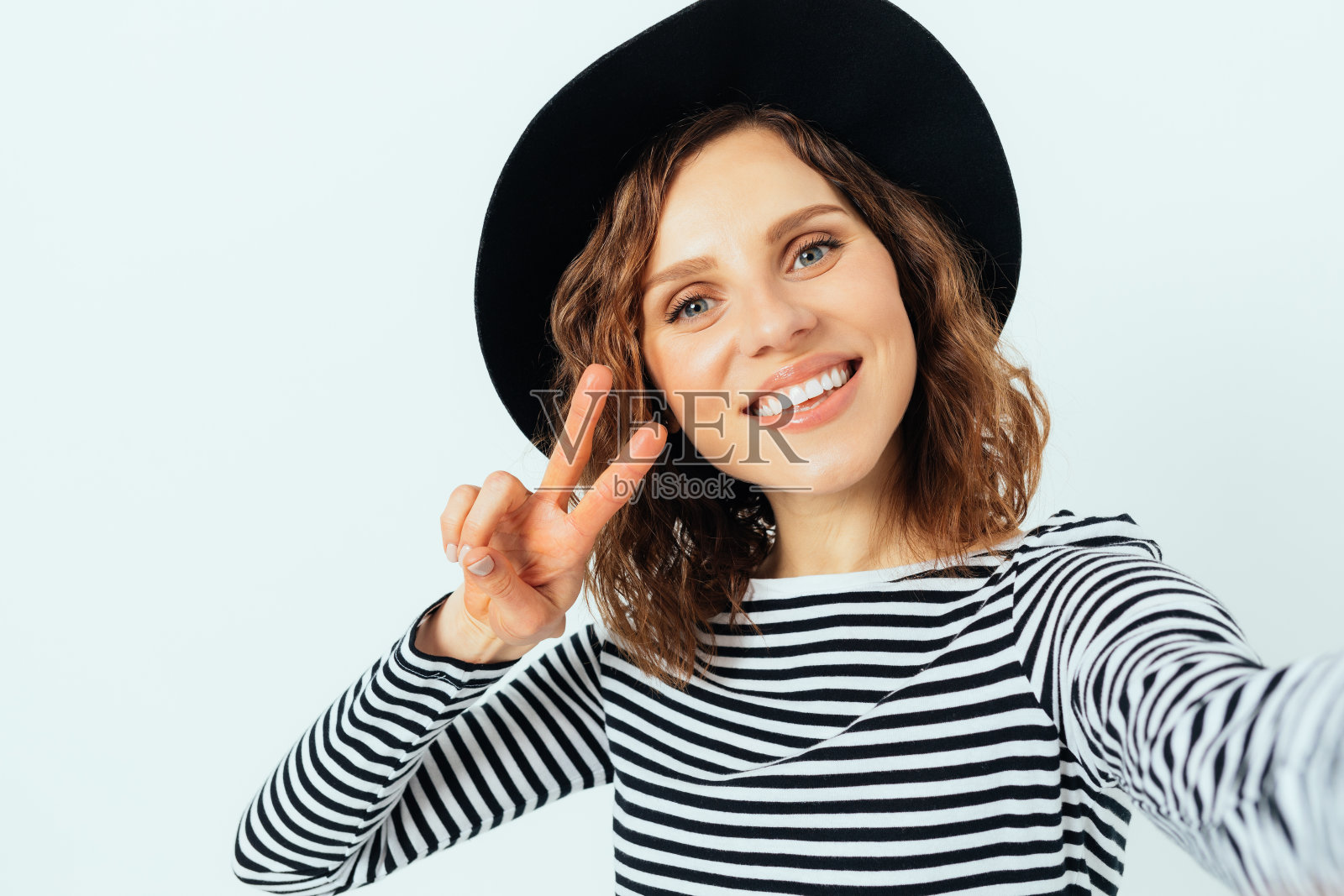 穿着黑色软呢帽和条纹衬衫的快乐美丽的年轻女子照片摄影图片