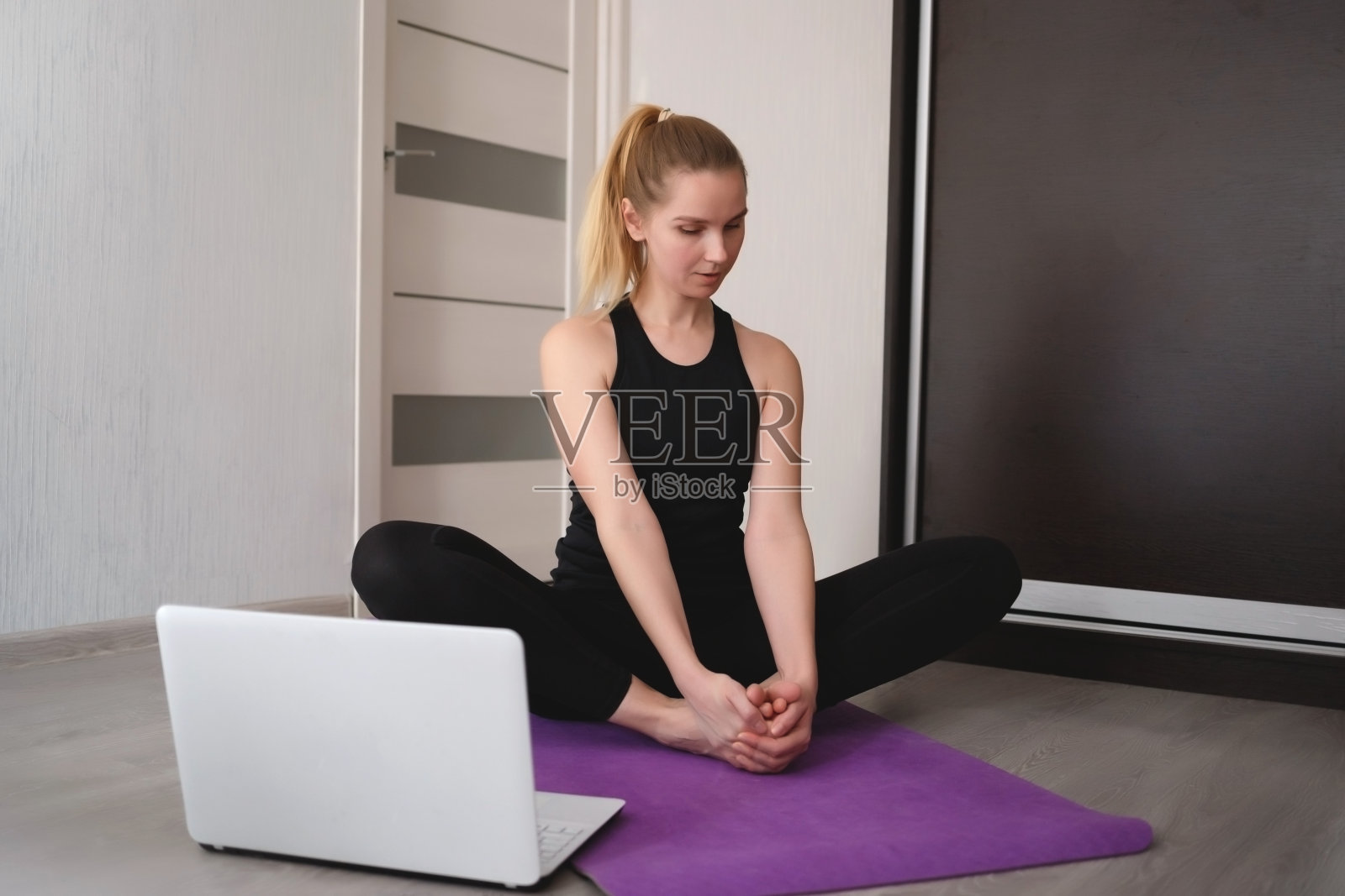 年轻女子在家里的瑜伽垫上做体式,在笔记本电脑前照片摄影图片