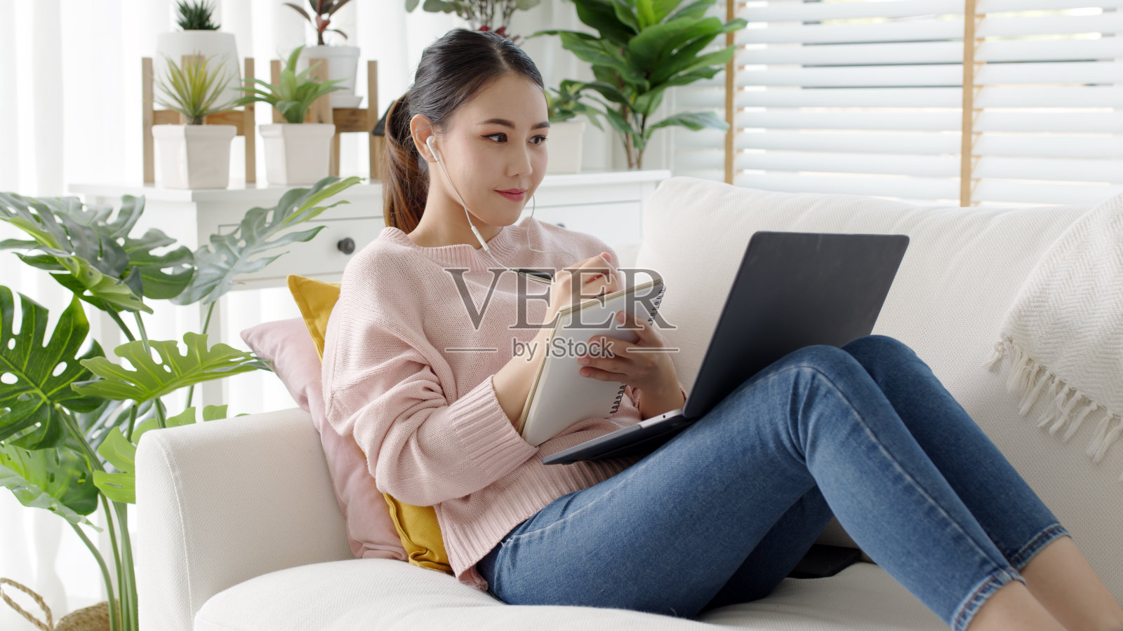 舒适放松年轻有魅力的亚洲女员工戴着耳机听数字在线课程发展计划在隔离社会距离在家里技能提升学校课程的职业道路。照片摄影图片