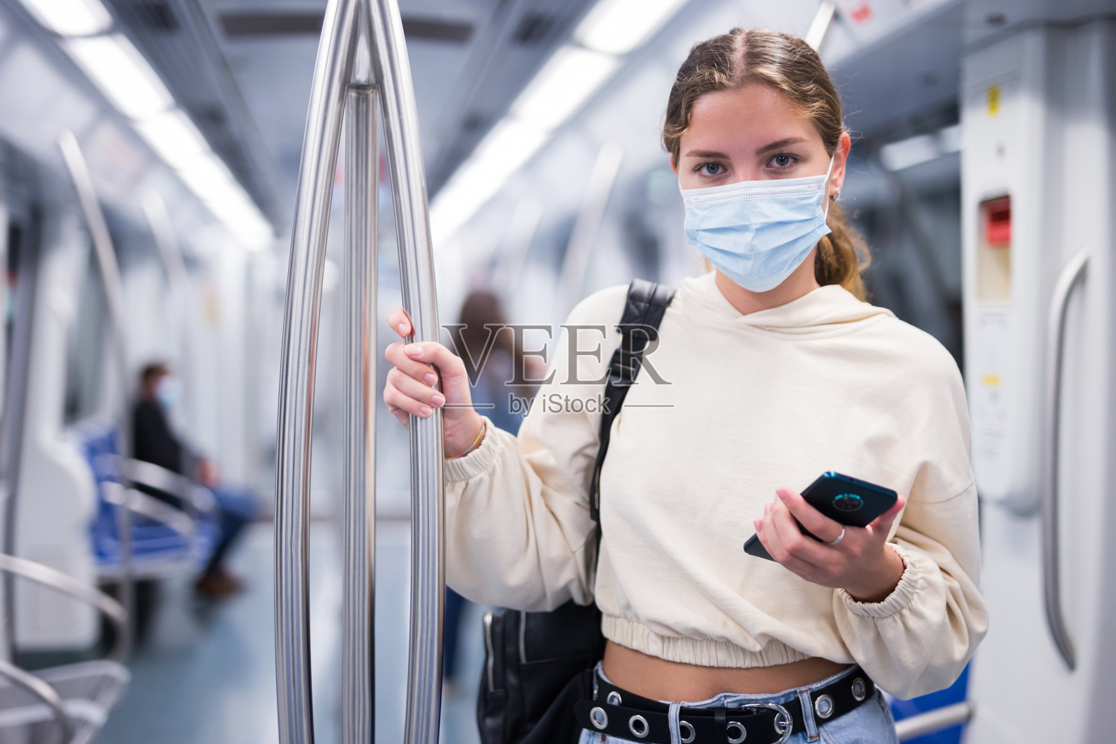 年轻女子戴着面具,带着手机在地铁乘火车旅行照片摄影图片