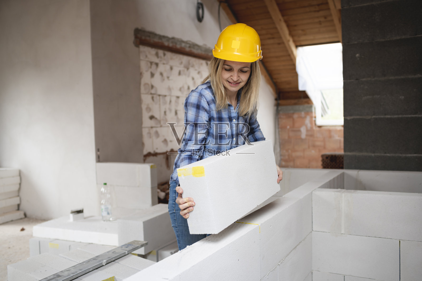 漂亮的年轻女工戴着黄色的安全帽在建筑工地工作,并竖起一堵墙照片摄影图片