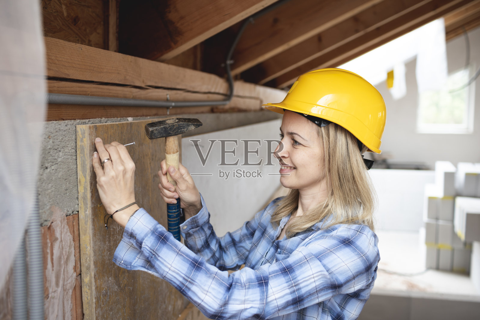 年轻漂亮的女工人穿着蓝色的工作服,戴着黄色的防护帽,手拿锤子在建筑工地工作照片摄影图片