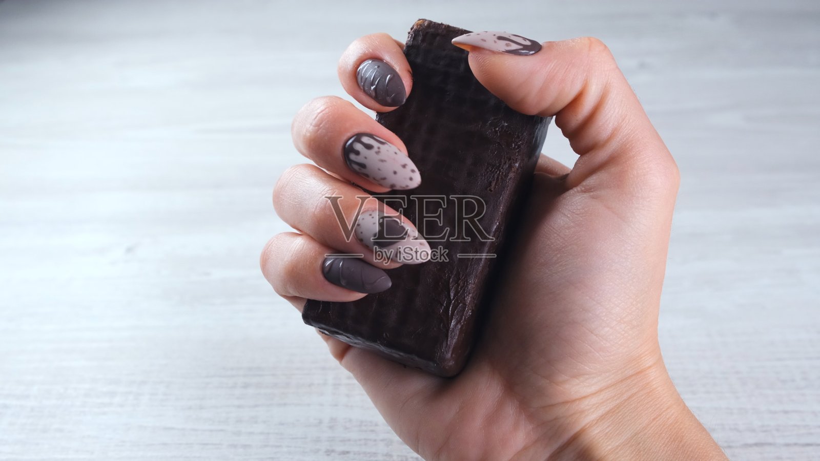 女性的手用美丽的棕色指甲在巧克力糖果的形式,拿着一个展开的黑巧克力棒,特写。喜欢甜点照片摄影图片