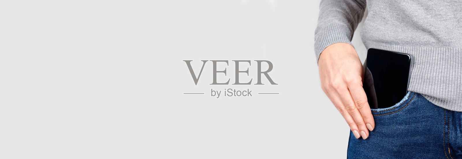 将手机放在灰色背景的牛仔裤口袋里。照片摄影图片