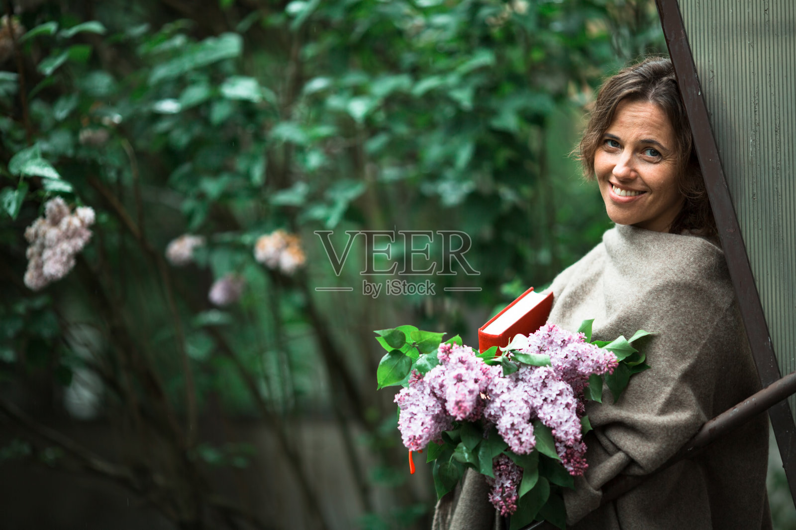 一个女人手里拿着一本书,在户外的绿树丛中。照片摄影图片
