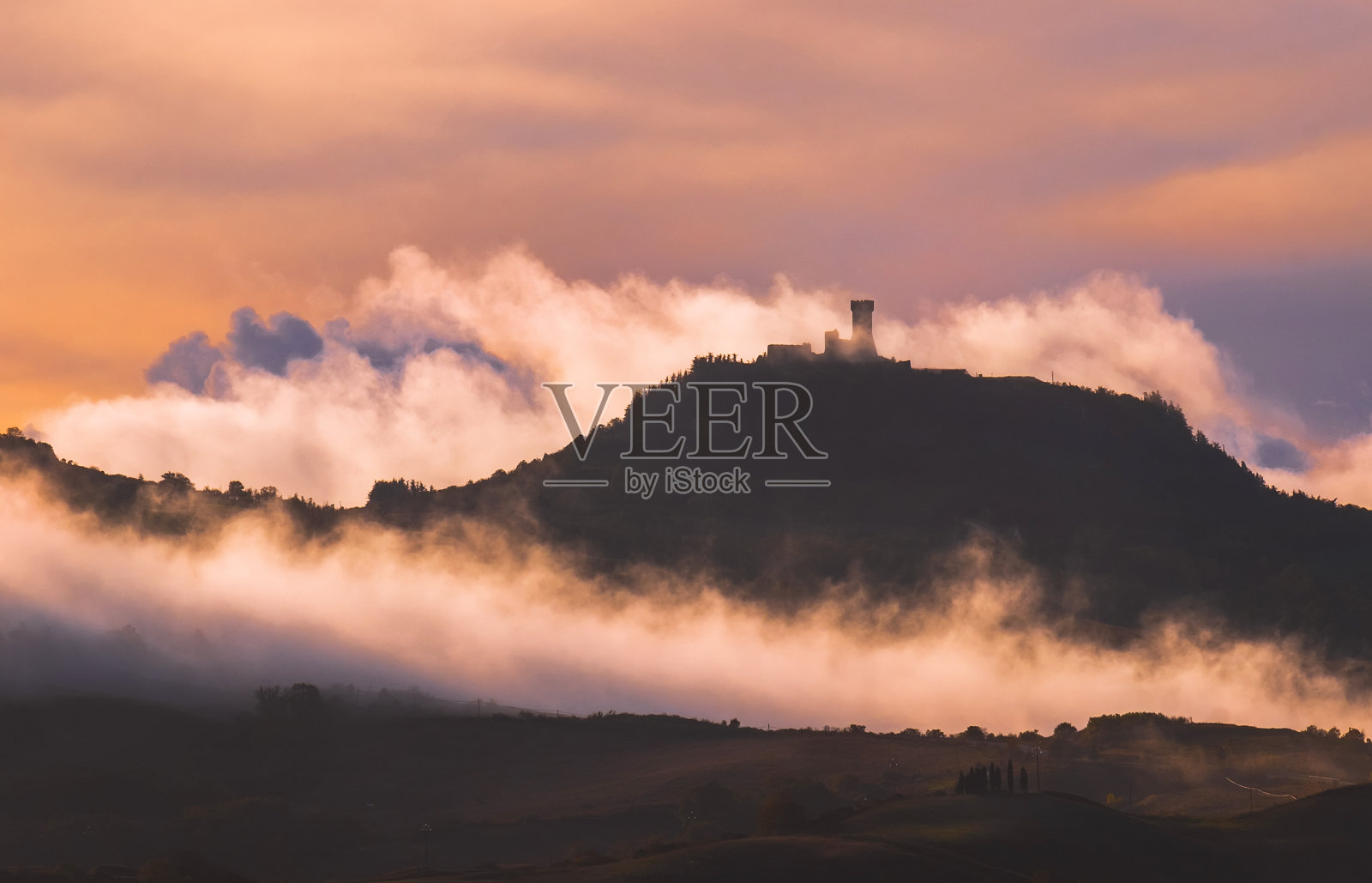 罗卡迪拉迪法尼主塔的防御工事覆盖着晨雾。日出的光线覆盖着卷曲的云运行在草地和田野,使光影在托斯卡纳山景观。照片摄影图片