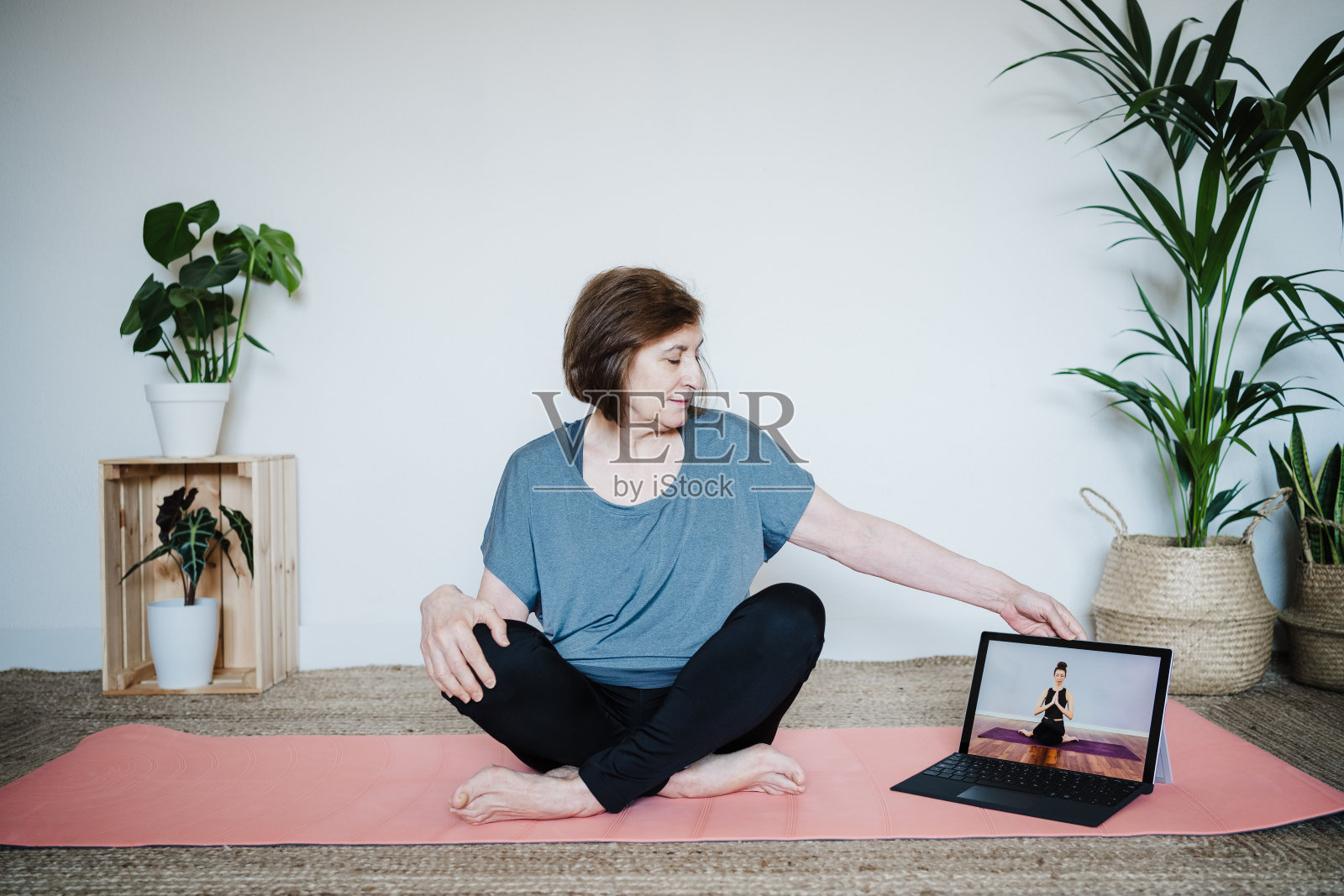 近距离观察成熟的白人年长的妇女在家里练习瑜伽姿势。使用笔记本电脑与老师在线上课。健康的科技生活方式照片摄影图片